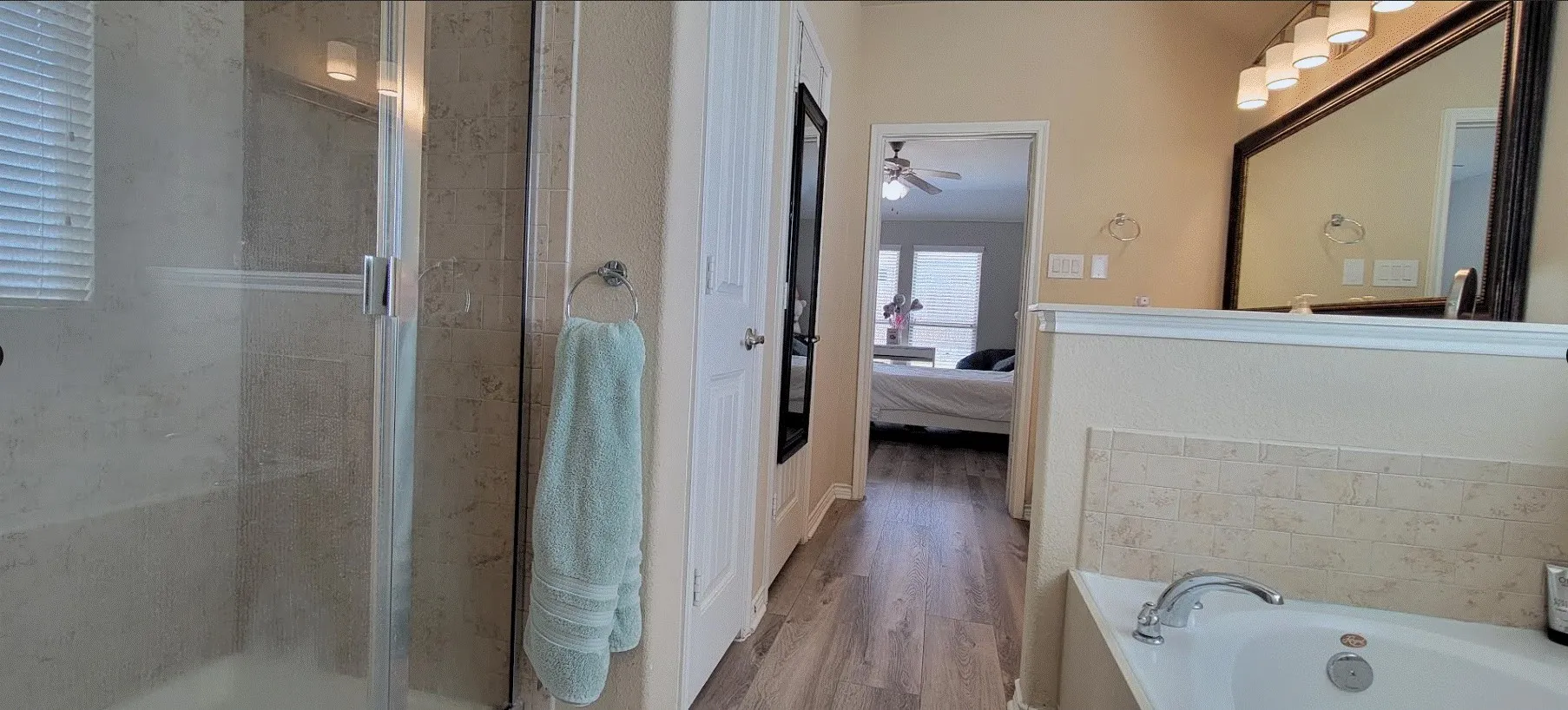 Bathroom featuring a built-in bathtub, a walk-in shower with clear glass enclosure, a vanity with a large framed mirror, and wood-finish flooring