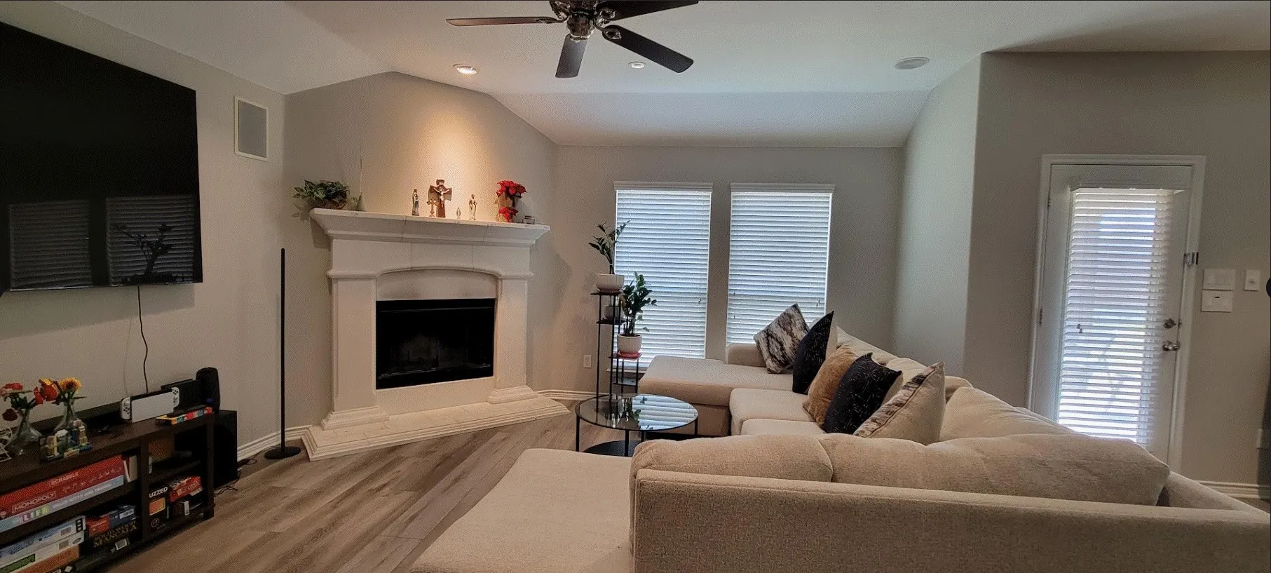 Living area featuring a corner fireplace with a cast stone mantel, wood-finish flooring, and a ceiling fan