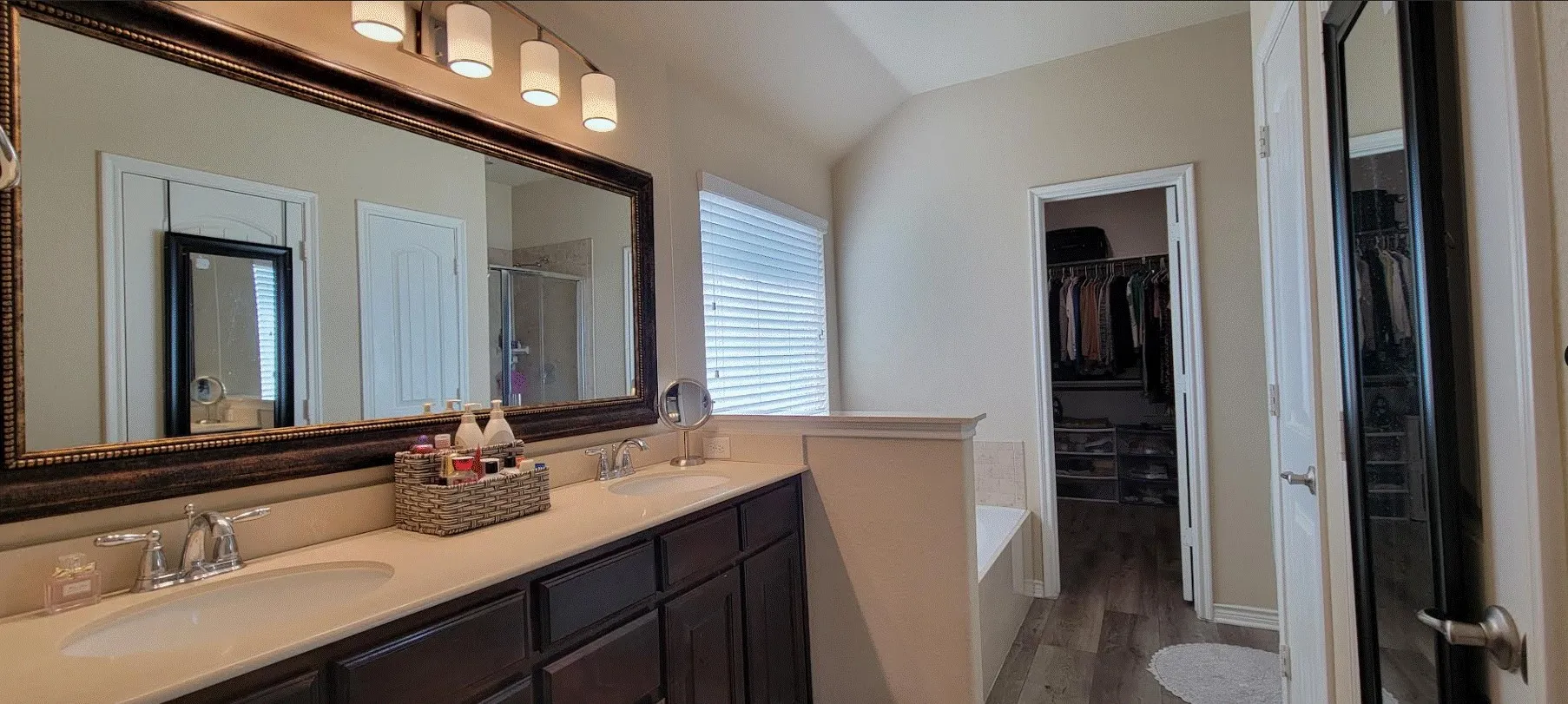 Spa-inspired primary bathroom featuring dual vanities with ample countertop space, a large framed mirror with integrated lighting, soaking tub, separate water closet, and tile flooring throughout