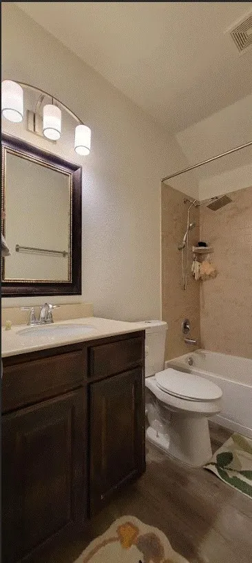Bathroom featuring a wood-finish vanity with an integrated sink, a rectangular mirror, and a shower-over-tub with tiled surround