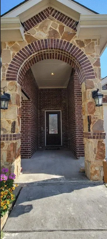 Brick and stone archway entry with exterior sconce lighting and a paneled door featuring decorative glass