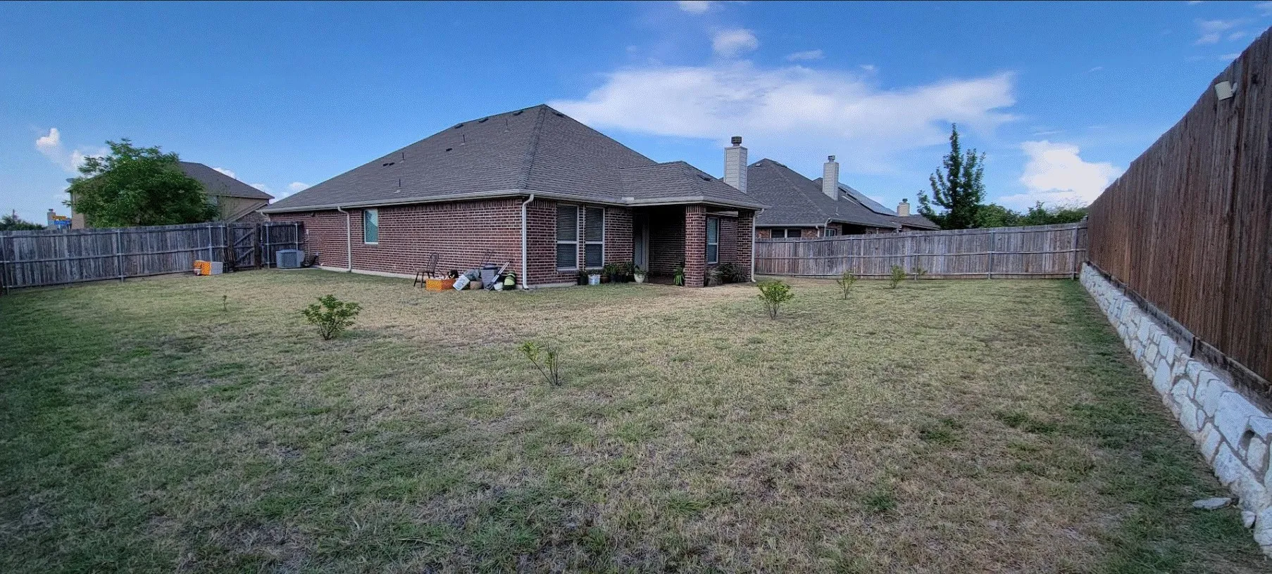 Expansive backyard featuring a manicured lawn, full brick exterior, covered patio, and wood privacy fencing with a stone base