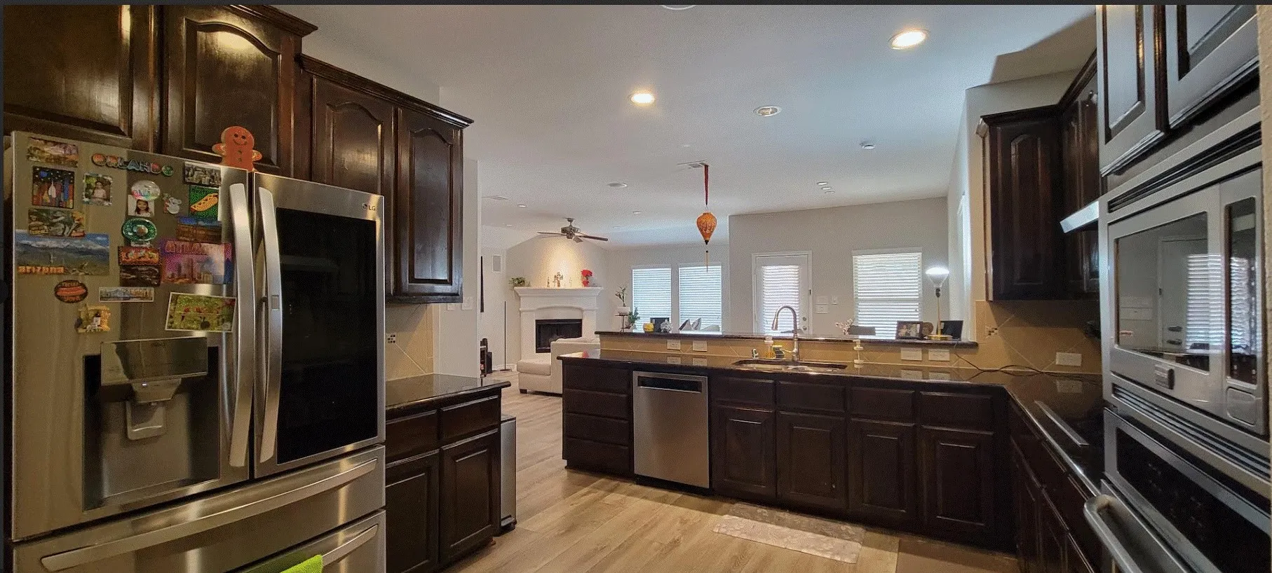 Kitchen featuring dark wood cabinetry, stainless steel appliances, wood-finish flooring, and a stone countertop