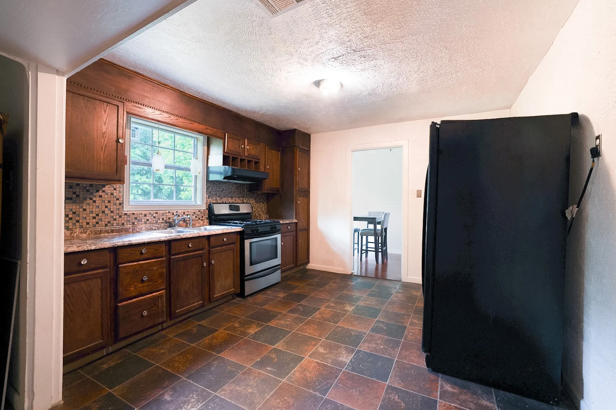 Kitchen featuring wood cabinetry, mosaic tile backsplash, stainless steel range, and checkerboard floor tiles