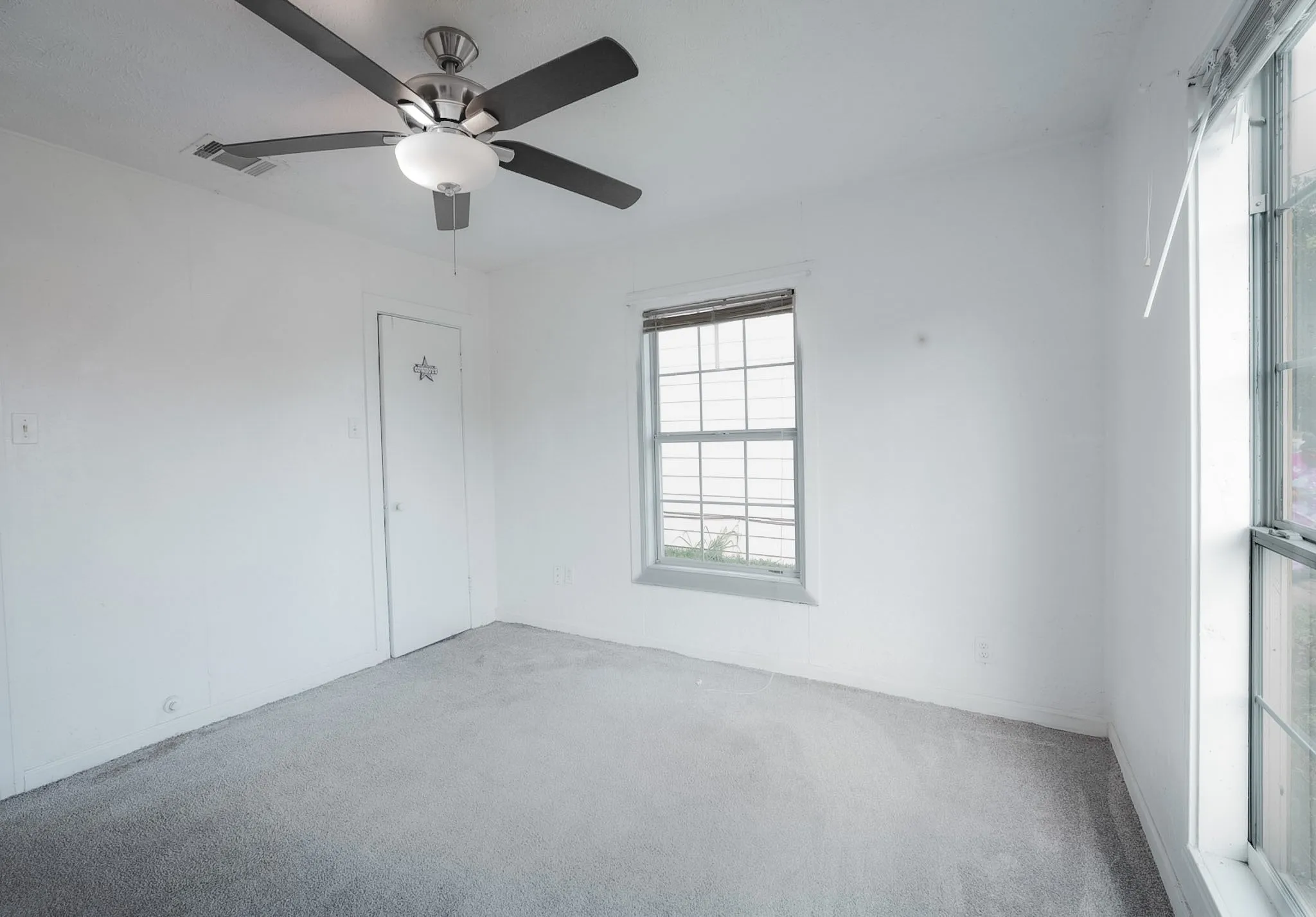 Recessed lighting, ceiling fan with light fixture, gray carpet flooring, white walls, and multiple windows providing ambient illumination