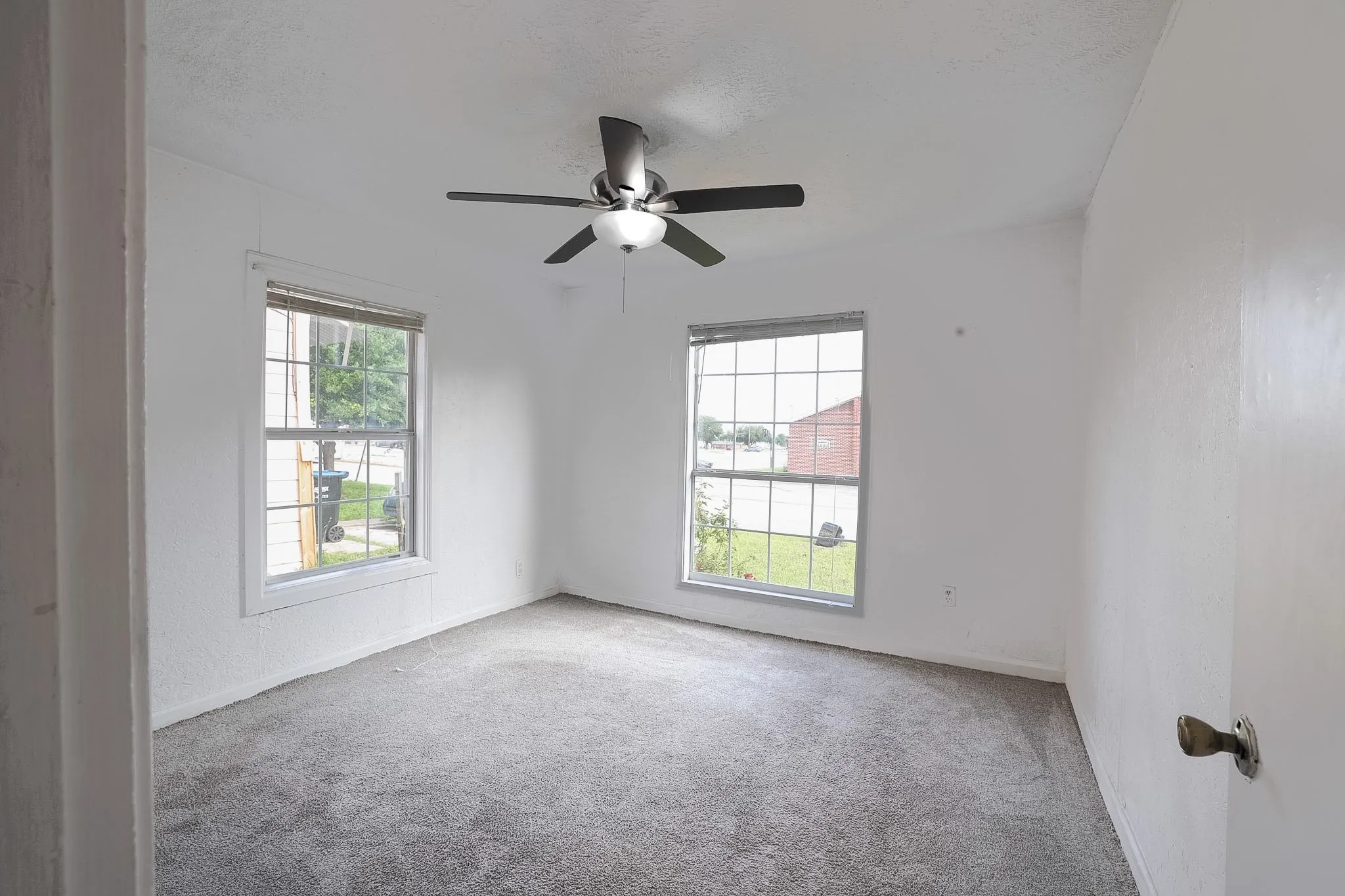 Carpeted room featuring two windows, a ceiling fan, and white painted walls