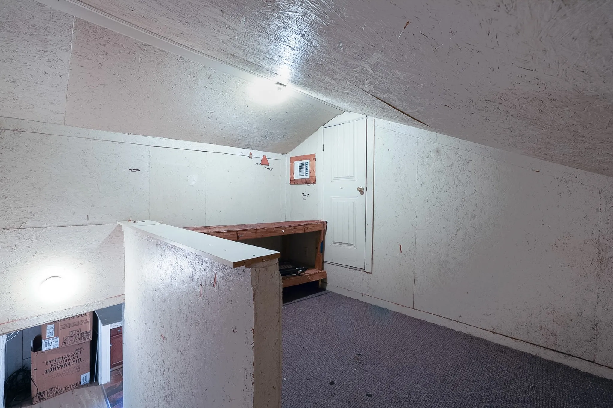 Sloping ceiling with recessed lighting, built-in wooden shelving, and a paneled door