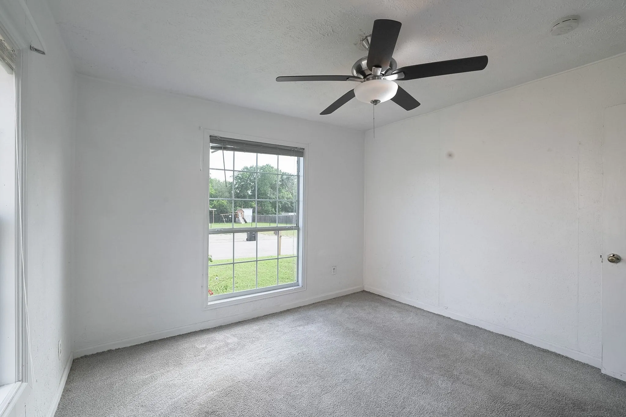Double-hung window, wall-mounted ceiling fan with integrated lighting, door with knob hardware, and neutral wall color