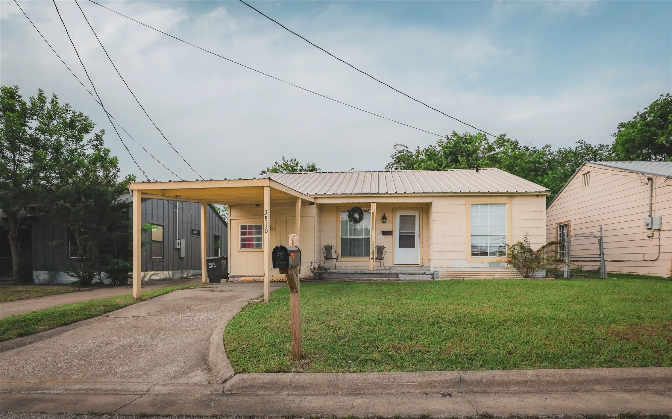 Front exterior with a metal roof, covered carport, concrete driveway, and a mailbox