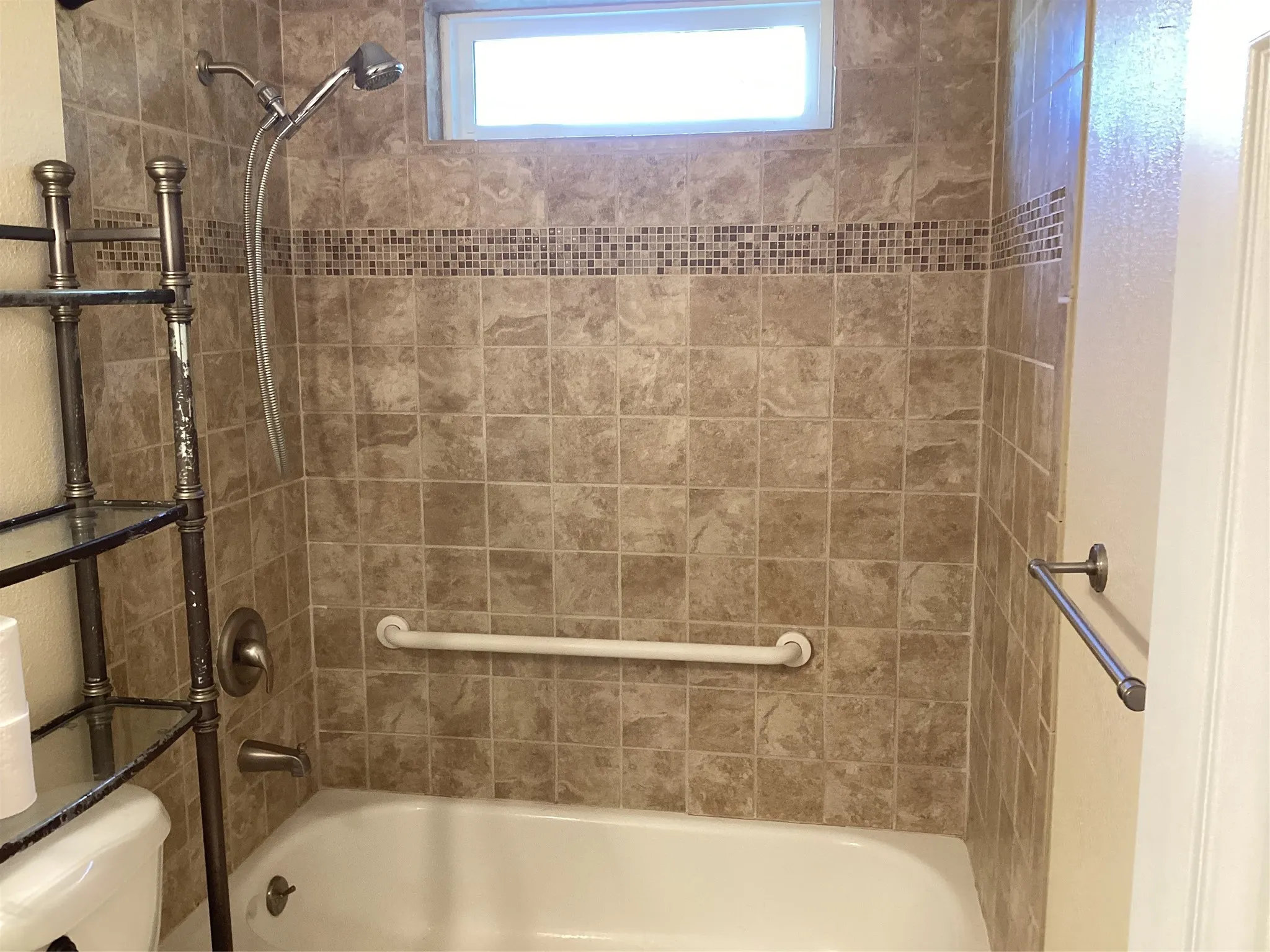 Bathtub with full-height tile surround, decorative mosaic tile accent, and a built-in grab bar
