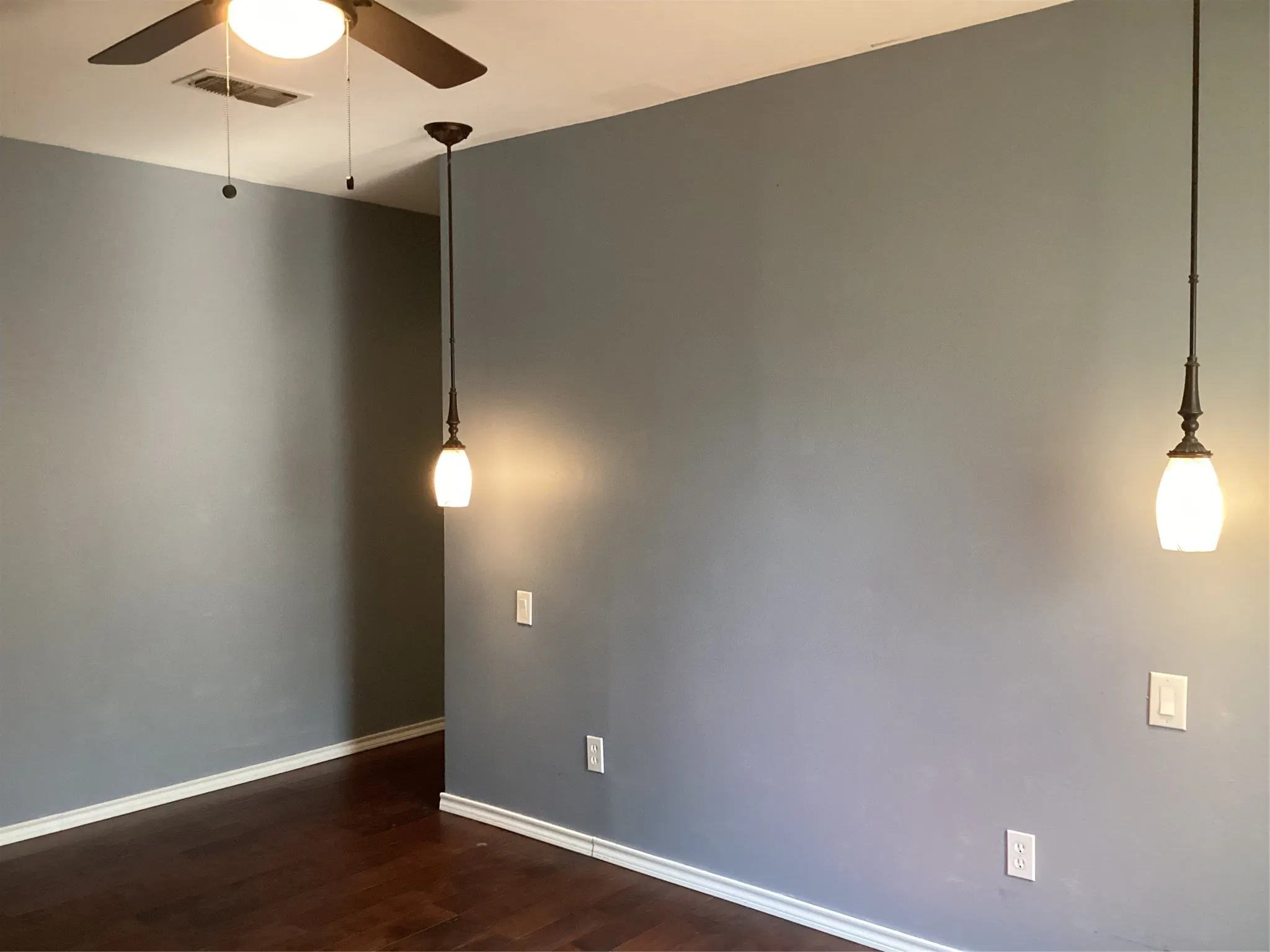 Wood-finish flooring with crisp white baseboards, complemented by a ceiling fan with integrated lighting and two pendant light fixtures