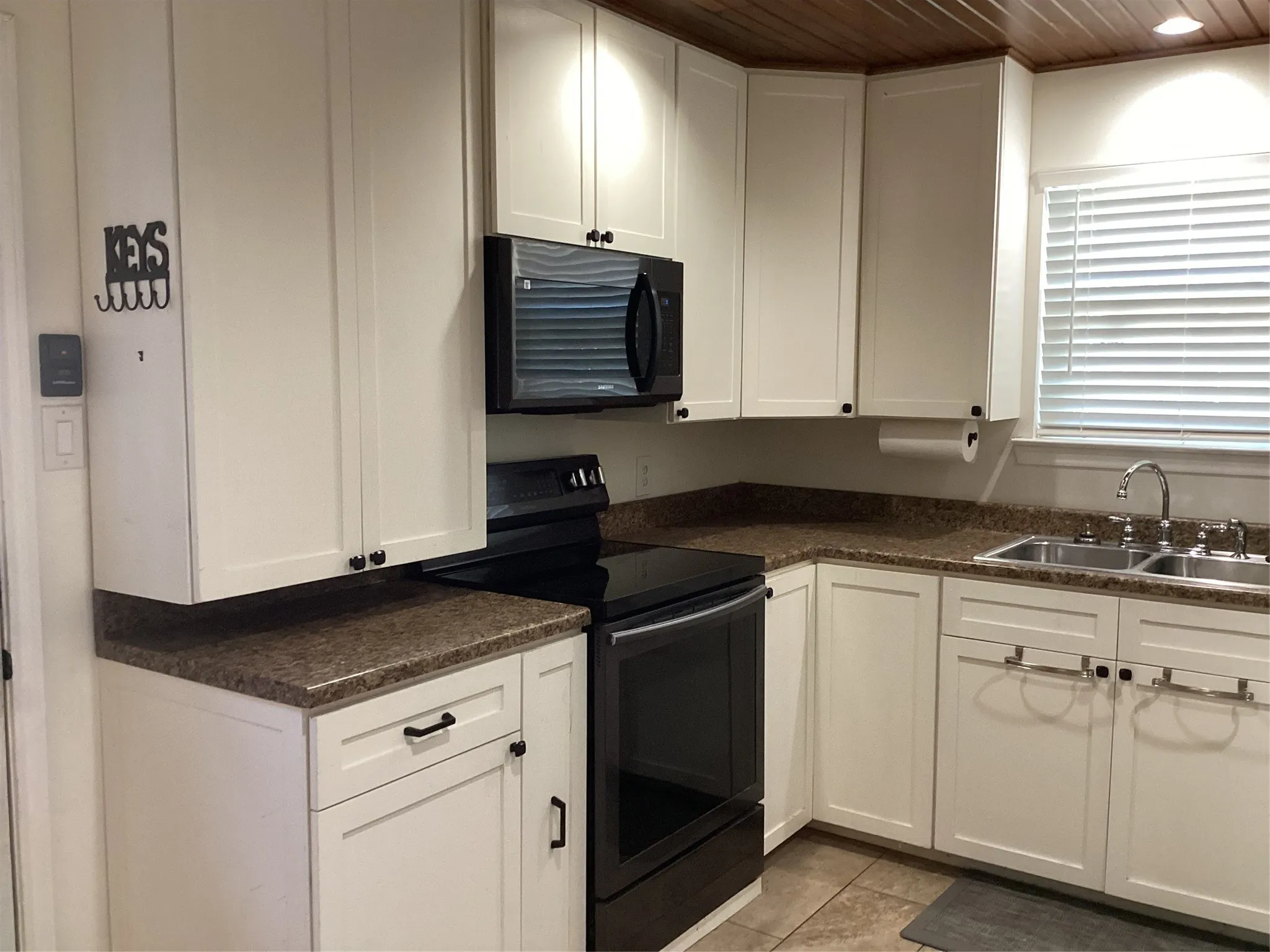 Kitchen featuring white cabinetry, dark countertops, a double basin sink, black appliances, and a wood-paneled ceiling