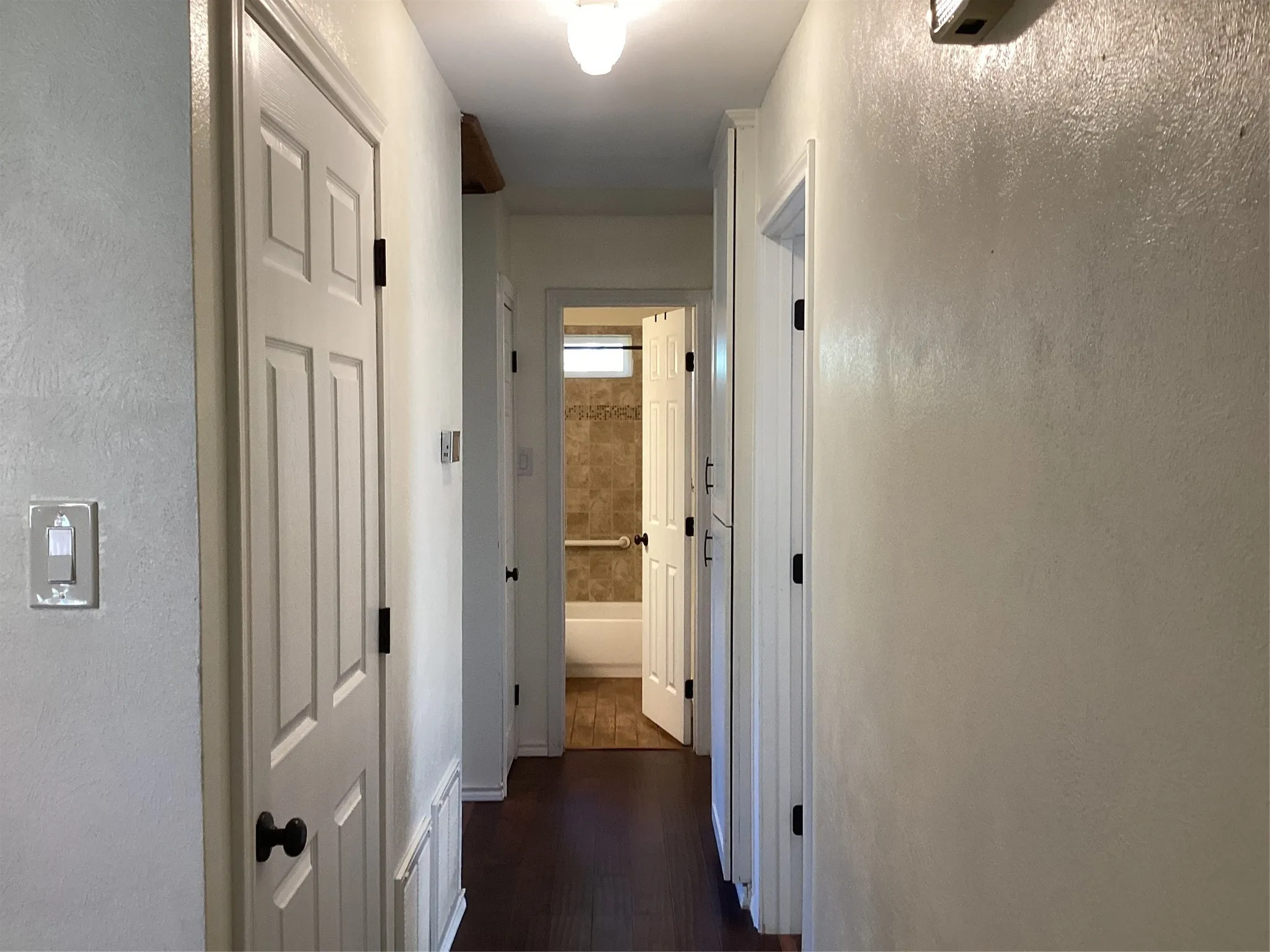 Hallway featuring white six-panel doors with black hardware, dark wood-finish flooring, and neutral textured walls with recessed ceiling lighting