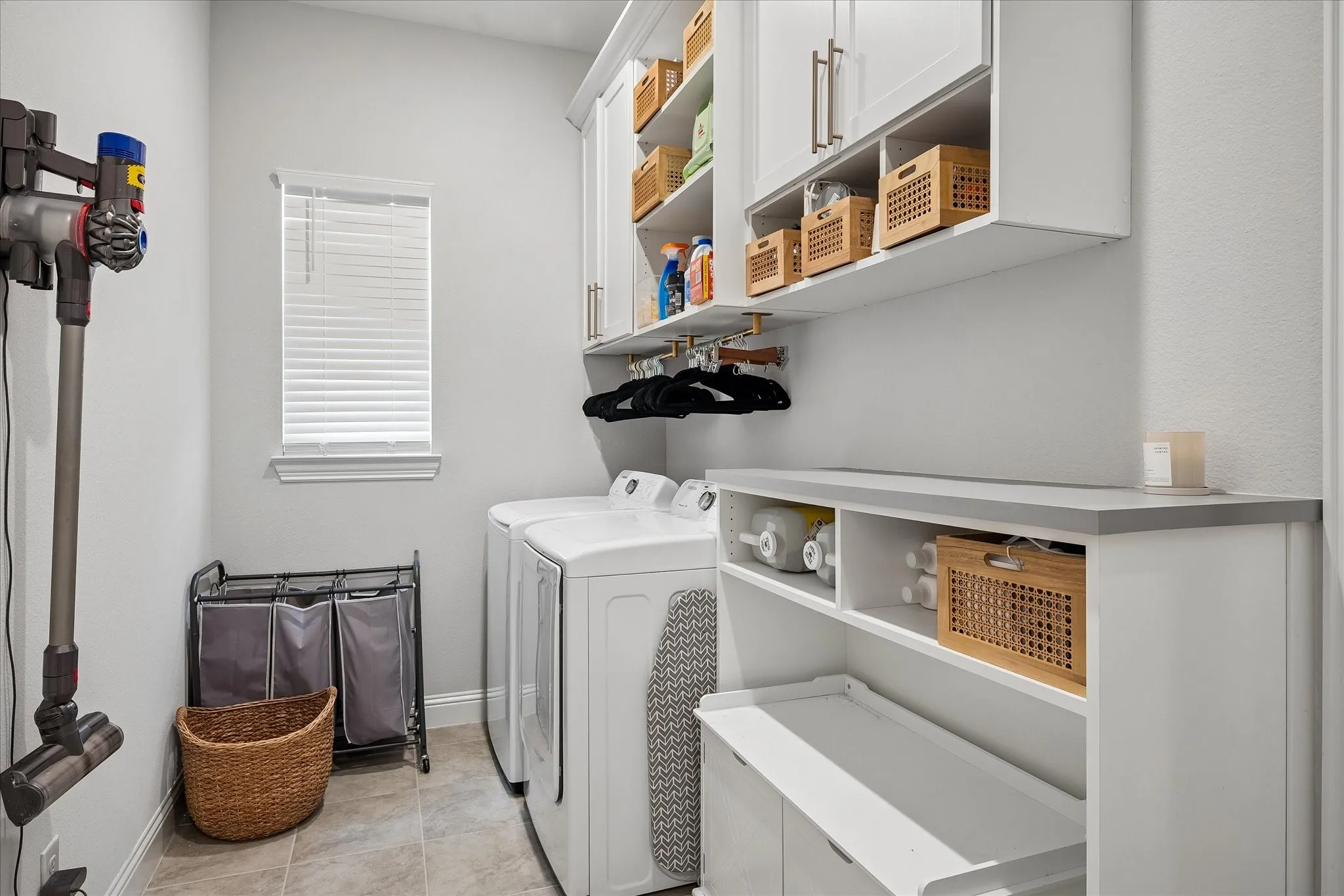 Dedicated laundry room featuring white cabinetry with open shelving, countertop workspace, and abundant storage for household essentials.
