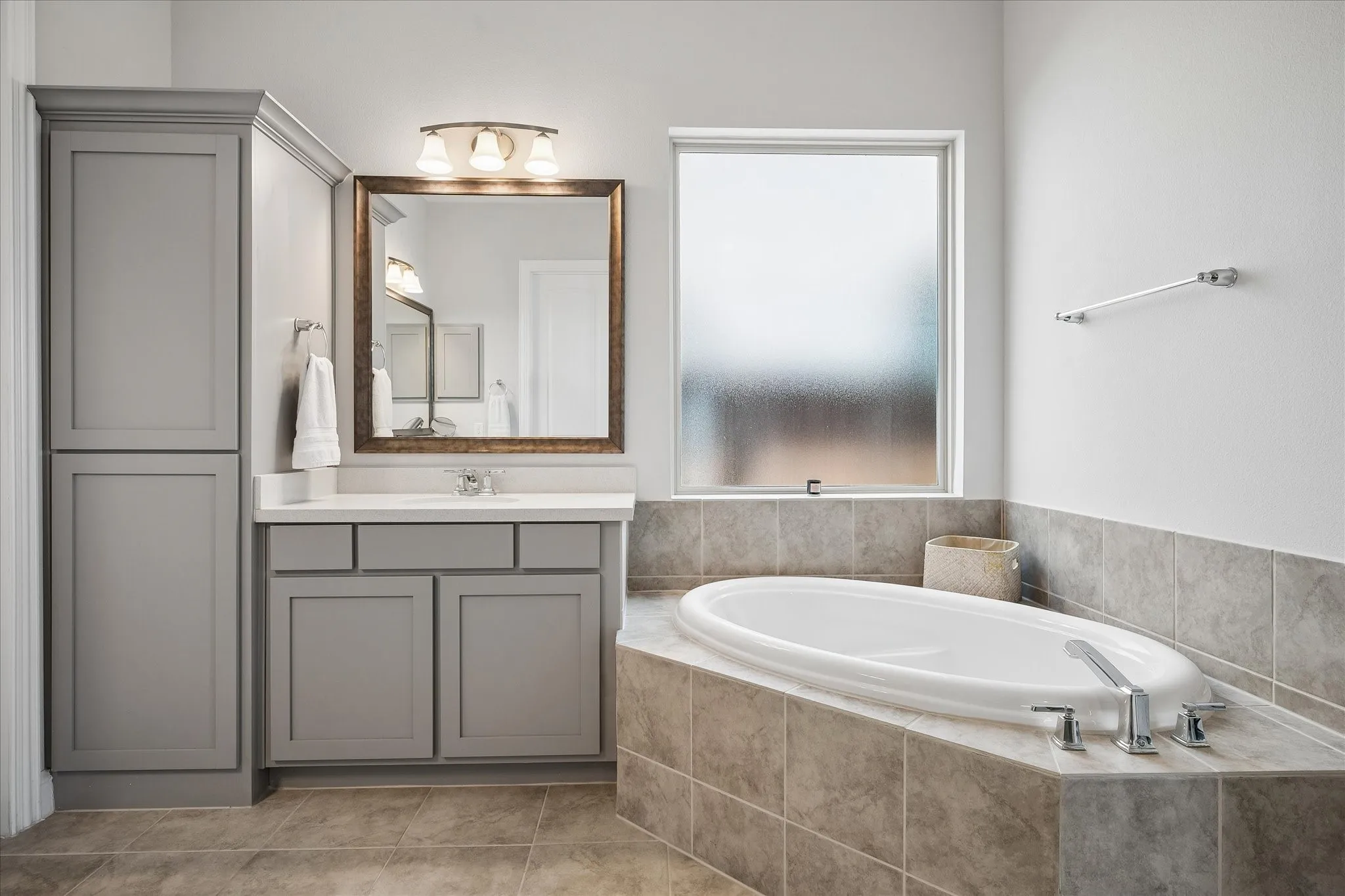 Spa-inspired primary bathroom featuring a soaking tub with chrome fixtures, gray tile surround, and neutral stone-finish flooring.