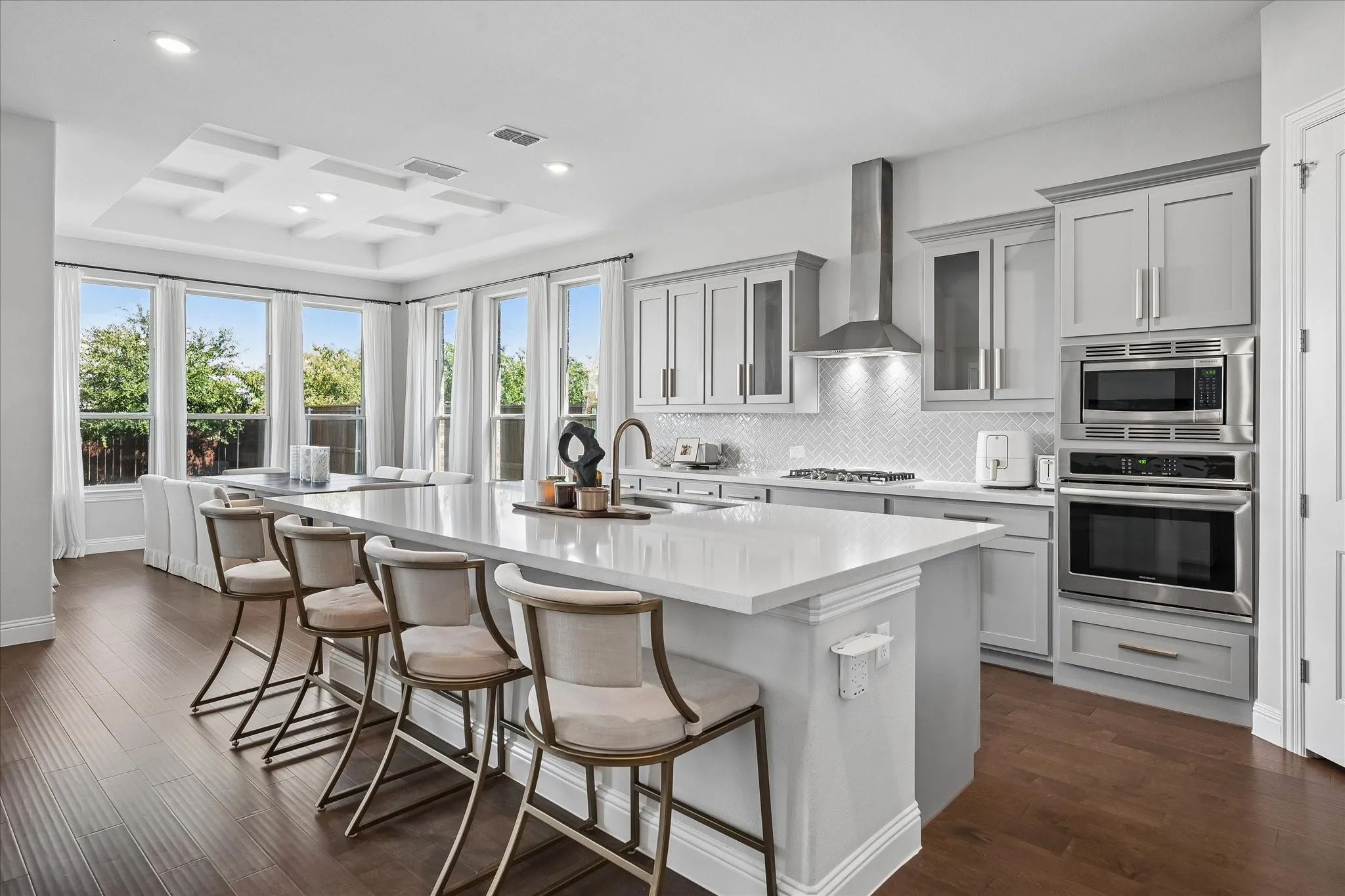 Gourmet kitchen featuring white cabinetry, a large waterfall-edge island with quartz countertop, stainless steel appliances including dual wall ovens and gas cooktop, and a professional-style range hood.