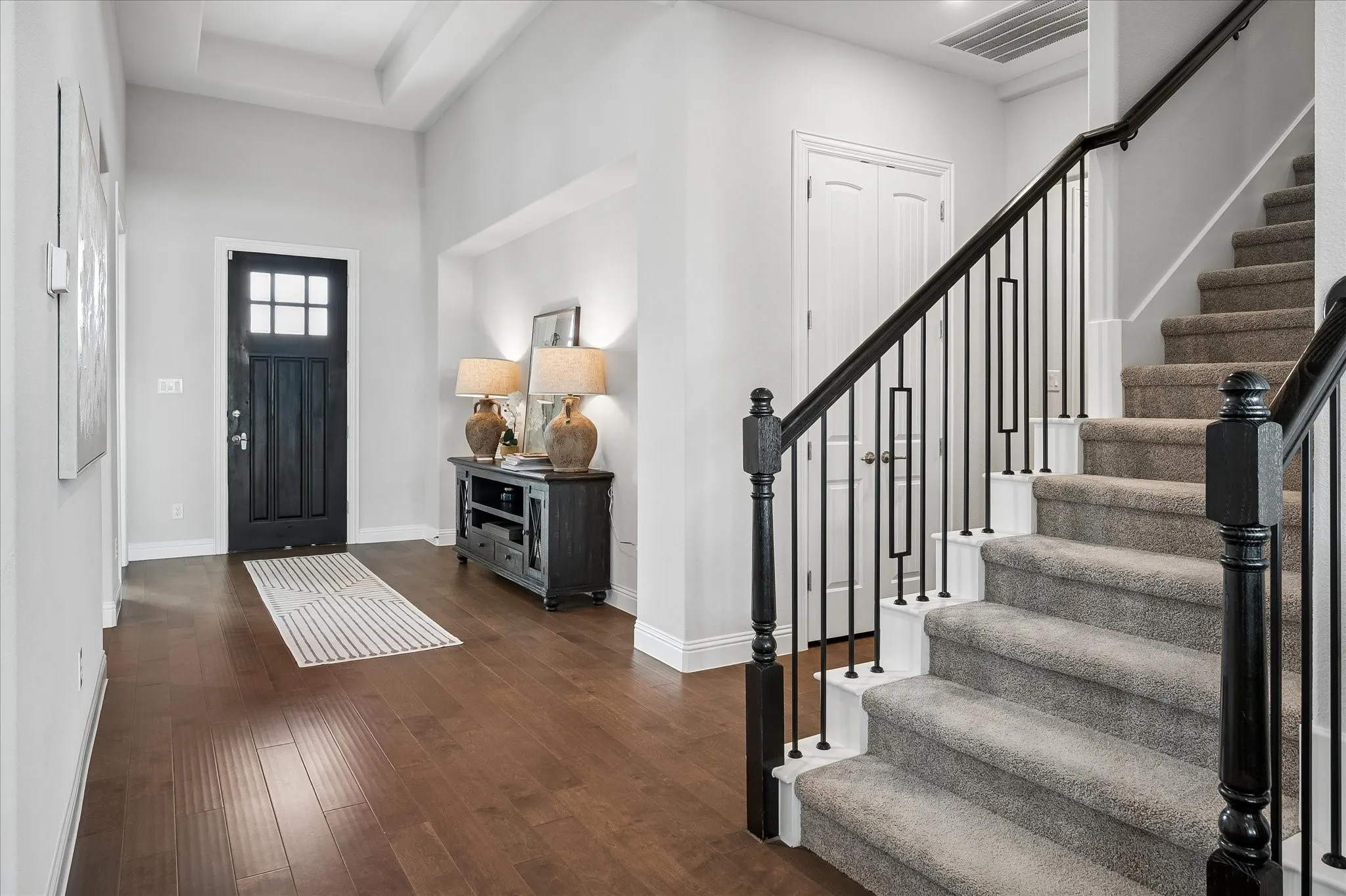 Welcoming foyer showcasing wood flooring, a black six-panel entry door with decorative glass panes and wrought iron accented stairway.