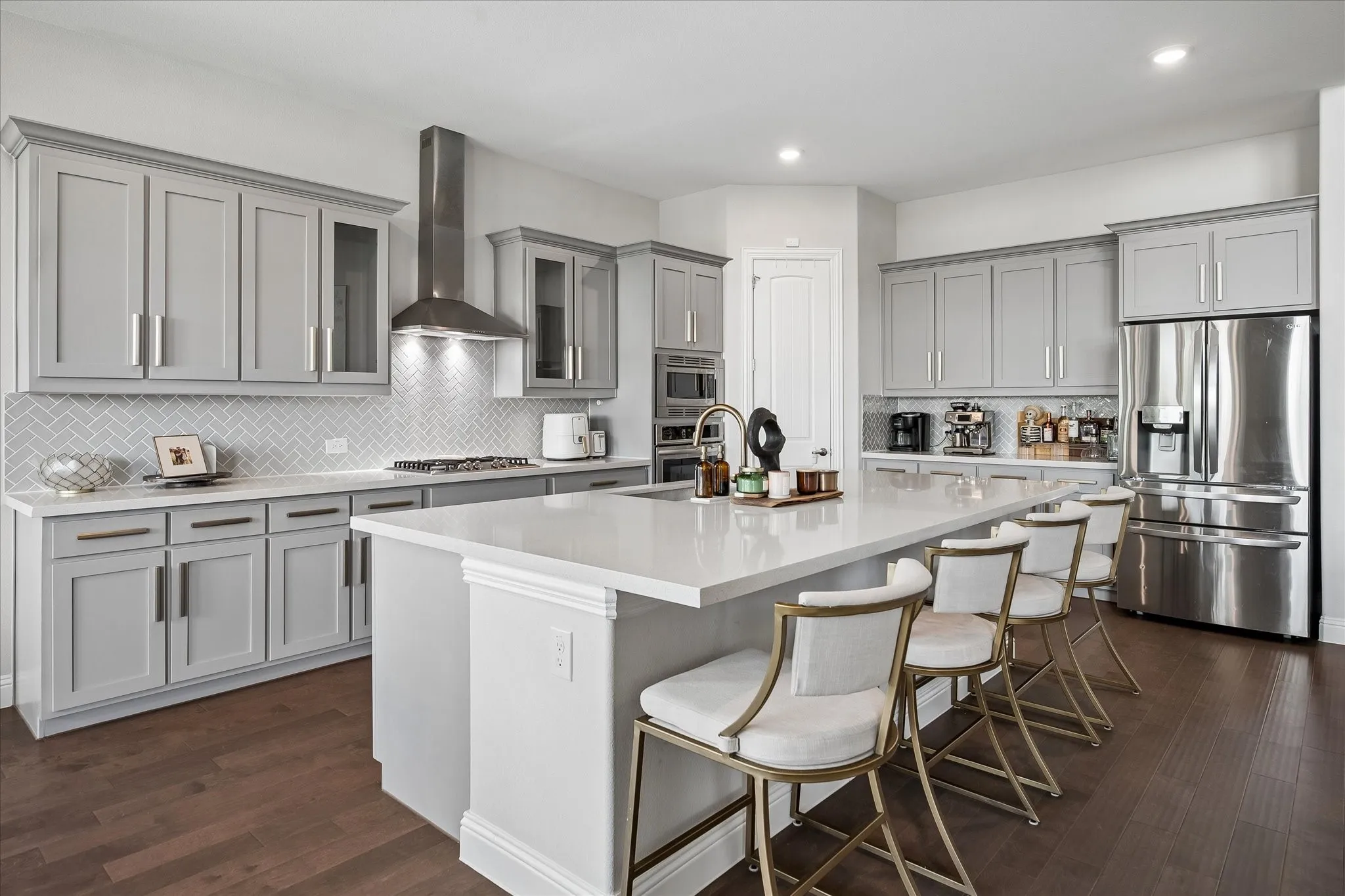 Kitchen featuring light gray cabinetry, white countertops, stainless steel appliances, a herringbone tile backsplash, and wood flooring.