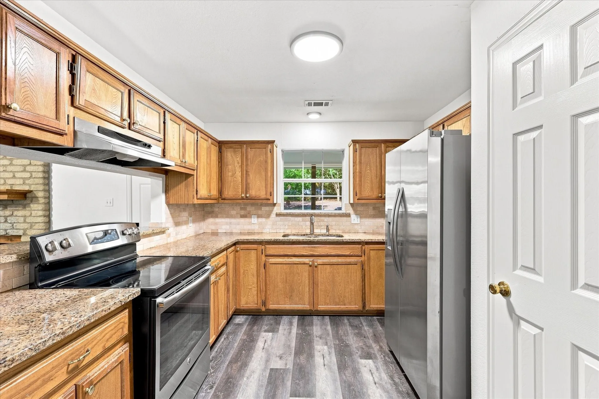 Kitchen featuring wood cabinetry, stone countertops, stainless steel appliances, and wood-finish flooring