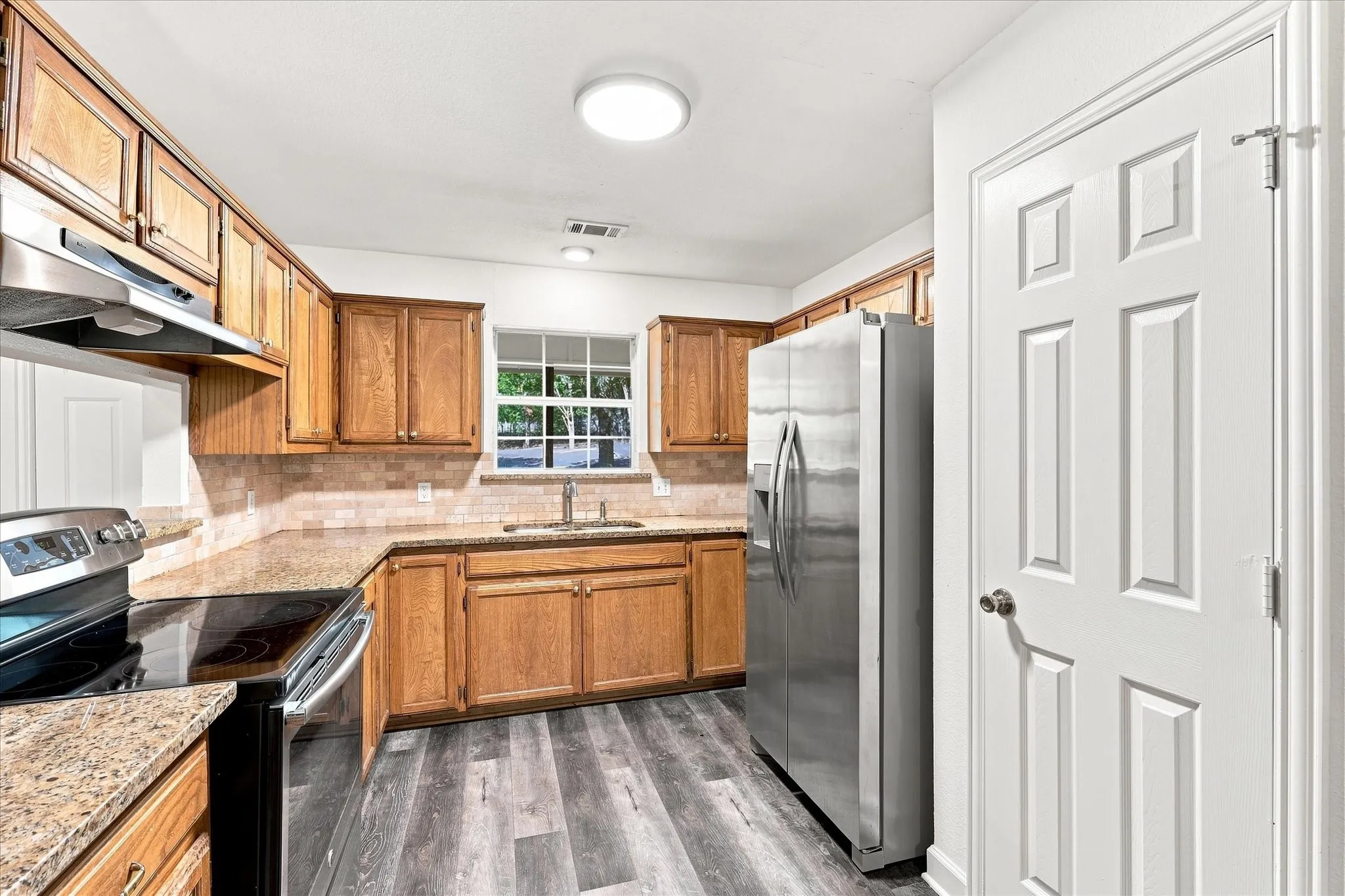 Kitchen featuring wood-finish cabinetry, stone countertops, stainless steel appliances, tile backsplash, and wood-look flooring