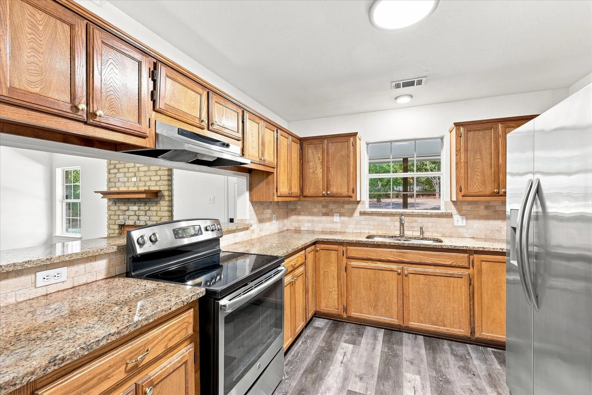 Wood-finish cabinetry, granite-style countertops, mosaic tile backsplash, stainless steel appliances, and wood-finish flooring