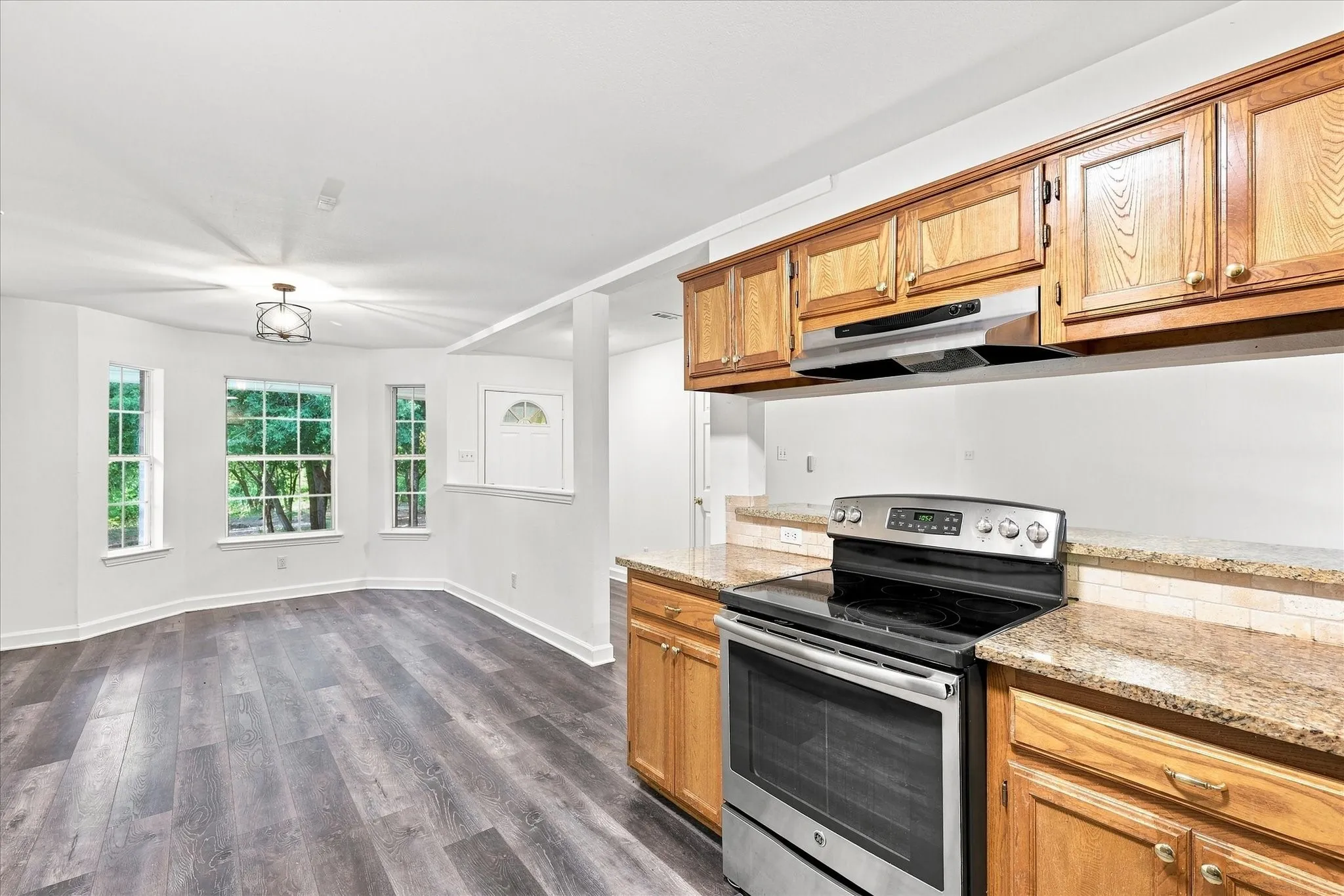 Wood-finish flooring, recessed lighting, and a contemporary ceiling fixture complement the stainless steel range and granite-style countertops