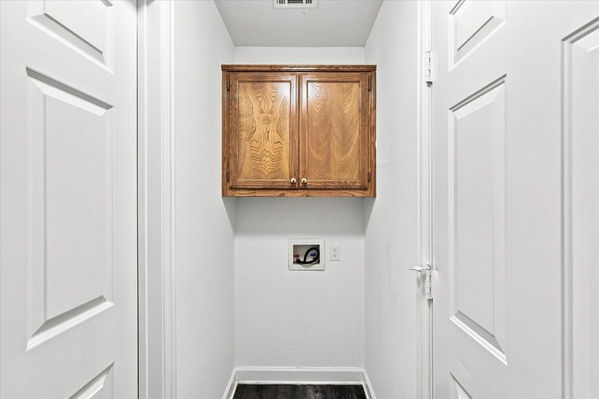 Dedicated laundry room featuring white panel doors, warm wood-finish cabinetry with dual-door upper storage, and practical utility outlet placement