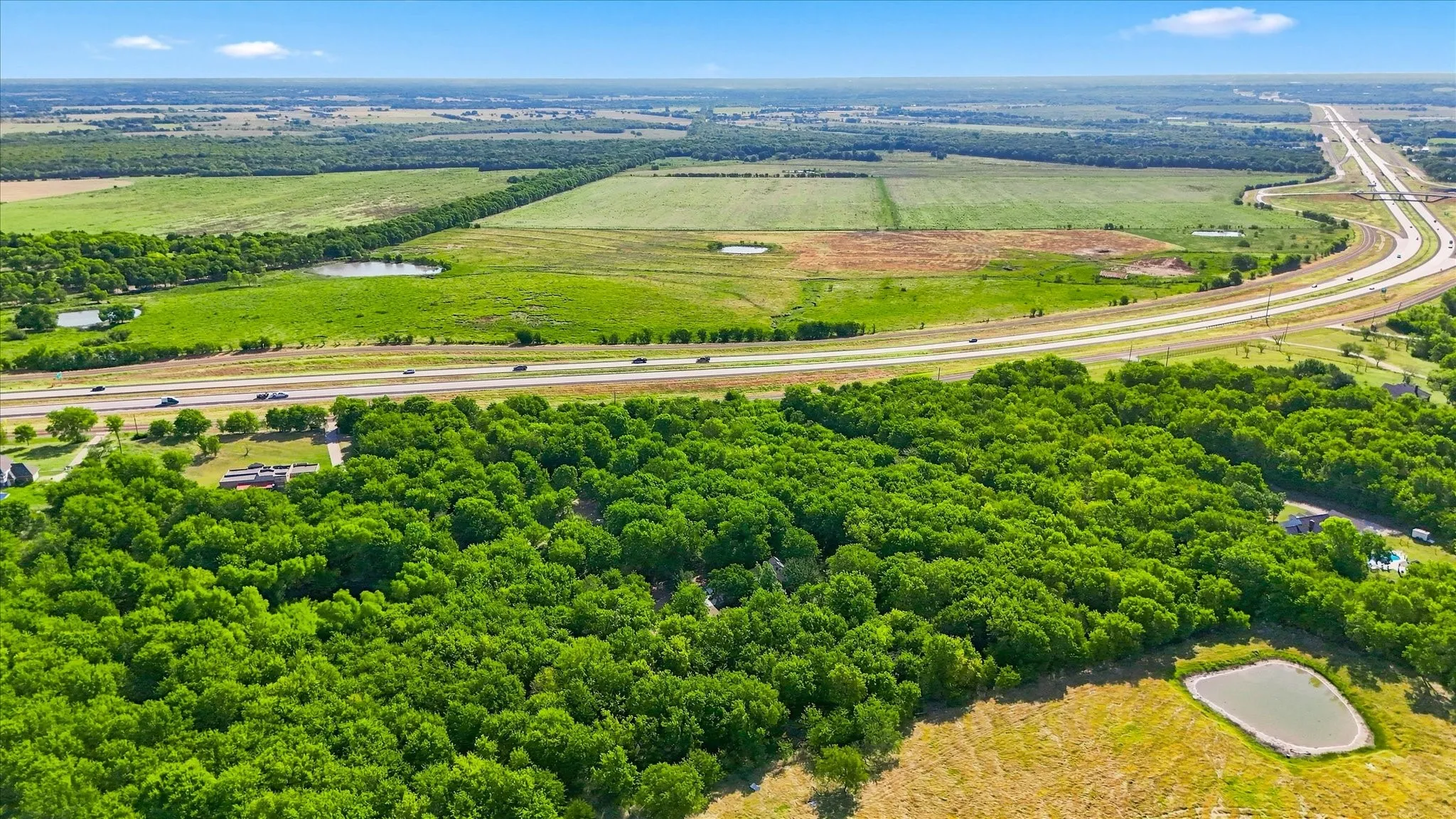 Expansive green landscape featuring mature trees, a highway, and multiple ponds