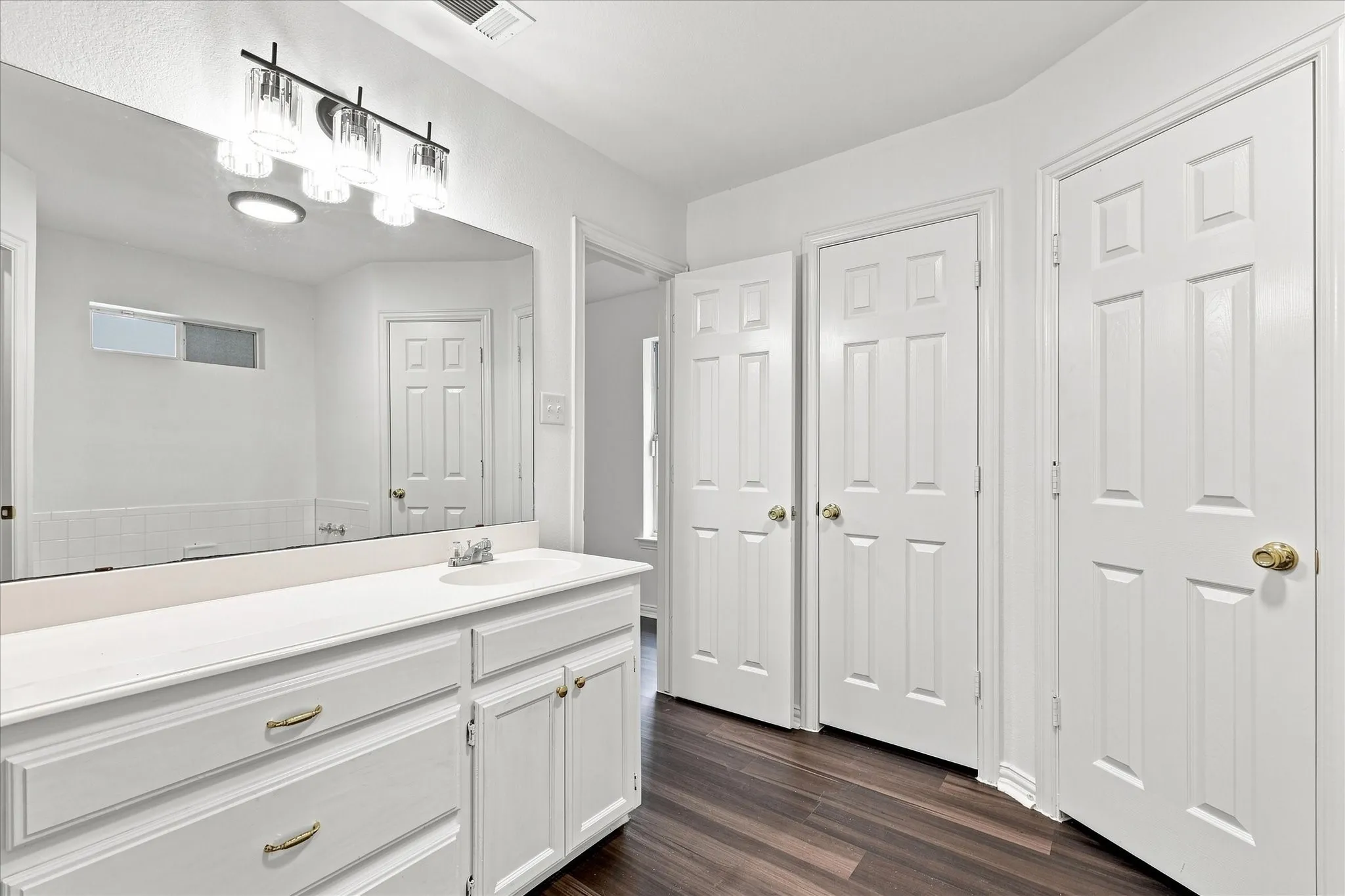 Spa-inspired primary bathroom featuring dual vanity with white cabinetry and brushed nickel hardware, extensive countertop workspace, and a large framed mirror with integrated lighting