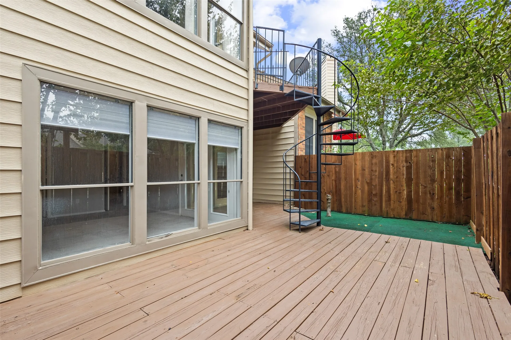 Wood plank decking, spiral staircase, horizontal wood fencing, and multiple windows with blinds