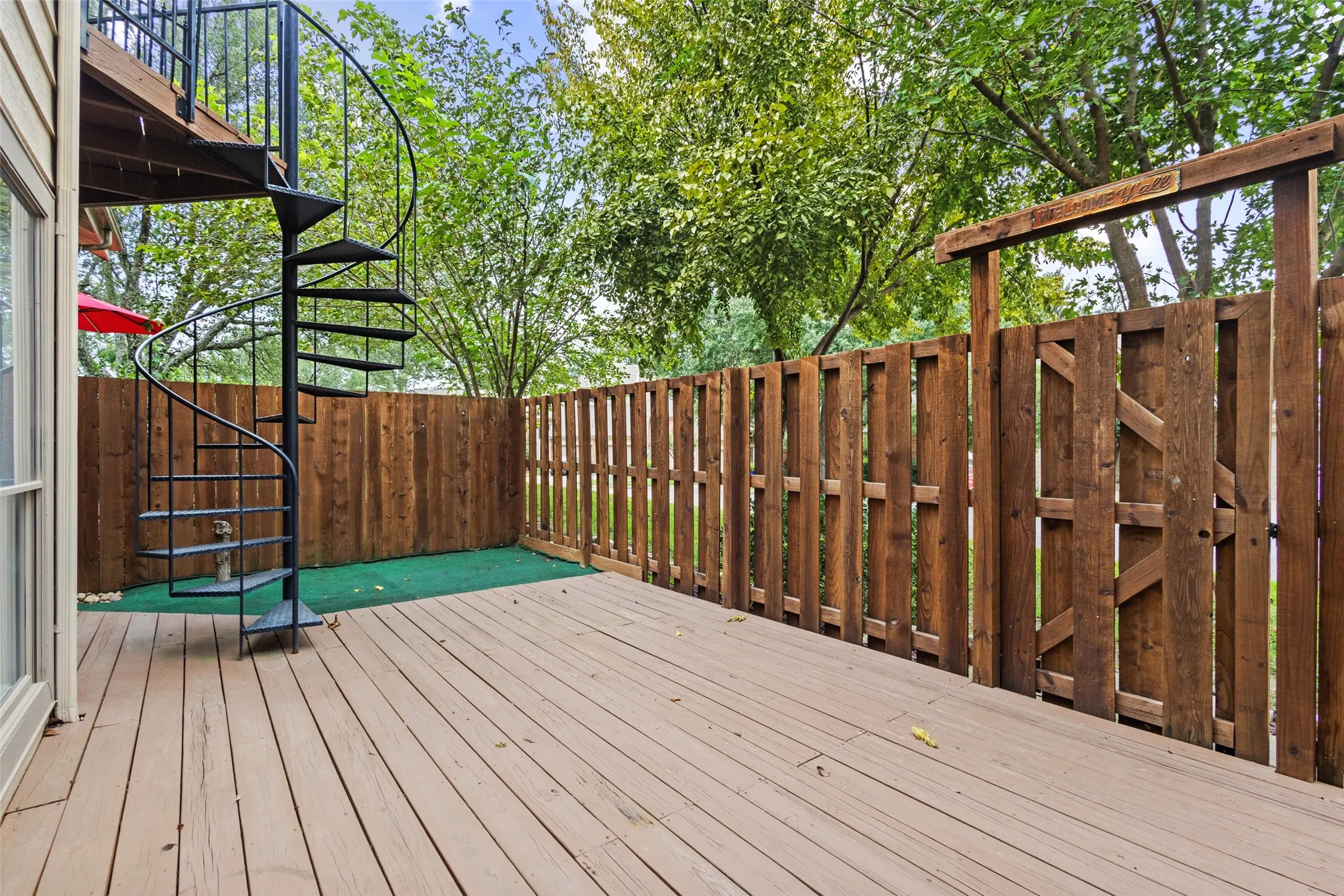 Expansive outdoor deck with wood-finish flooring, a black spiral staircase, and a tall privacy fence
