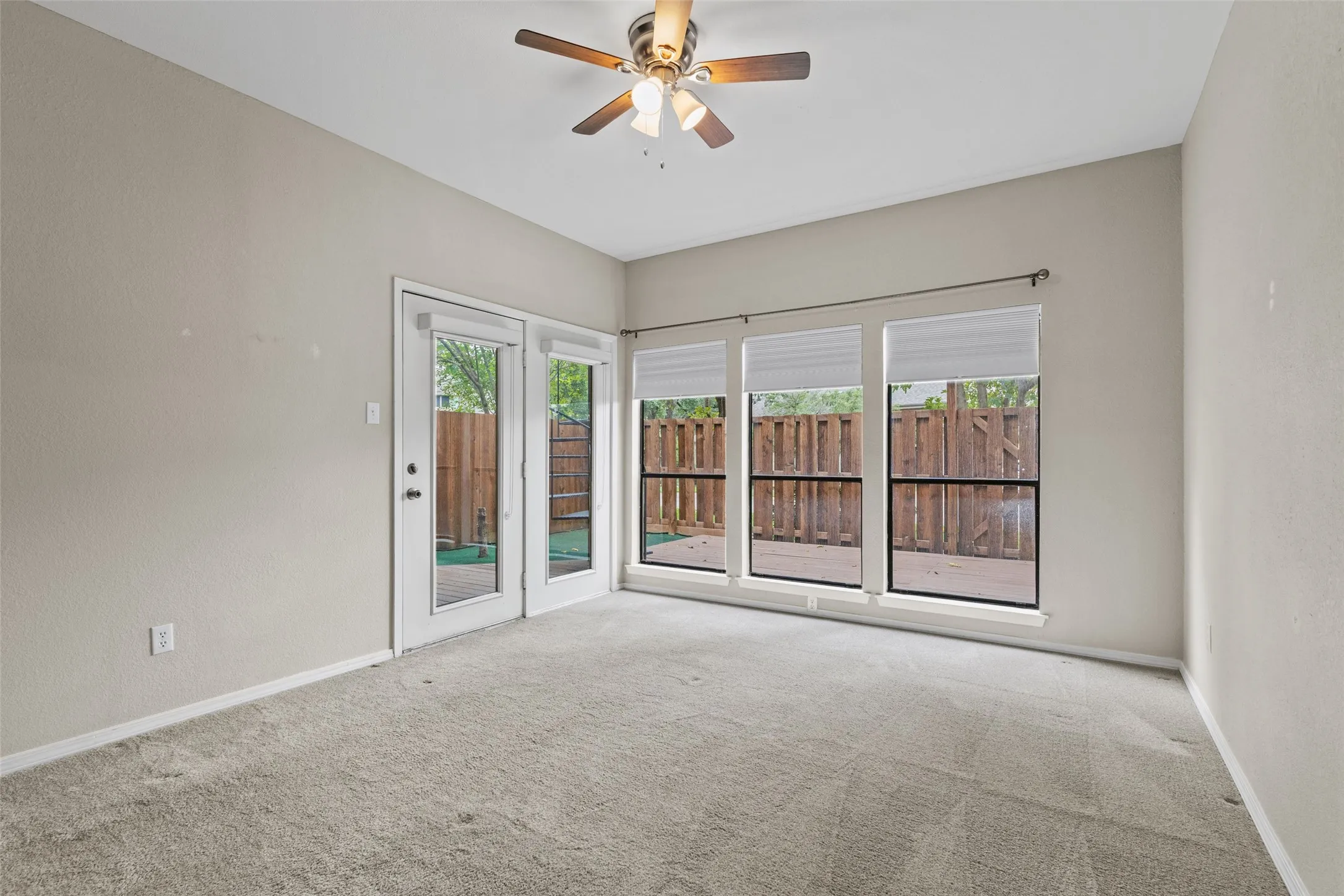 Neutral wall tones, carpeted flooring, a ceiling fan with light fixture, and multiple windows with blinds
