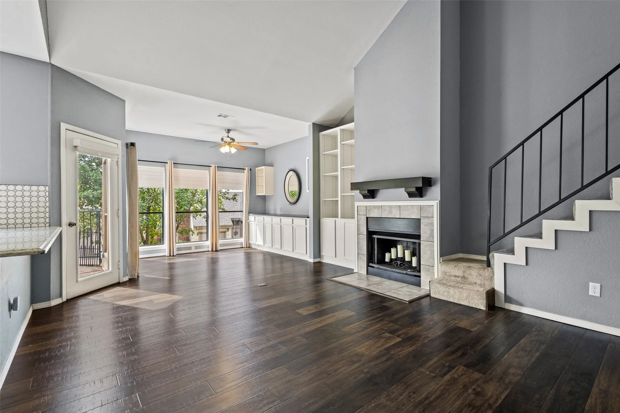 Spacious living area featuring dark wood-finish flooring, a tiled fireplace with a built-in mantel, and large picture windows