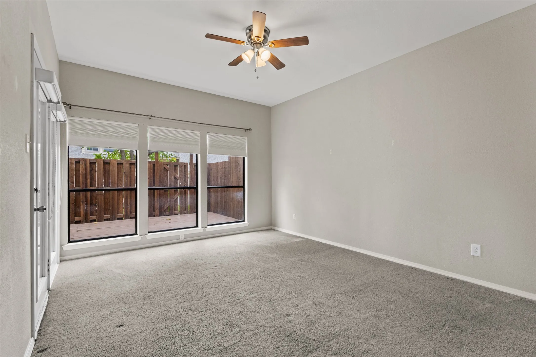 Vaulted ceiling with a ceiling fan, three large windows with blinds, and light gray wall paint