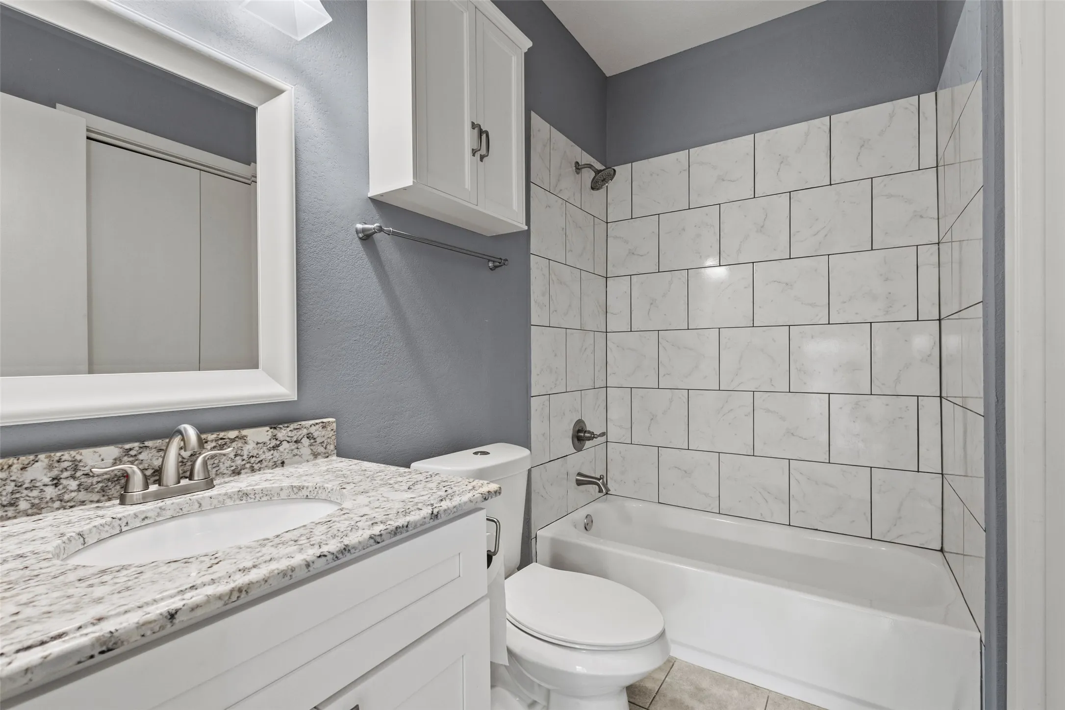 White shaker-style vanity with a light-colored stone countertop and an undermount sink
