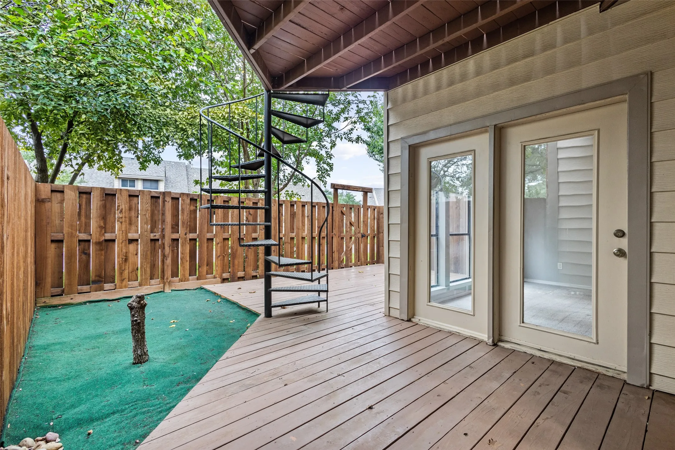 Outdoor deck with wood-finish planks, a black spiral staircase, and a wood privacy fence