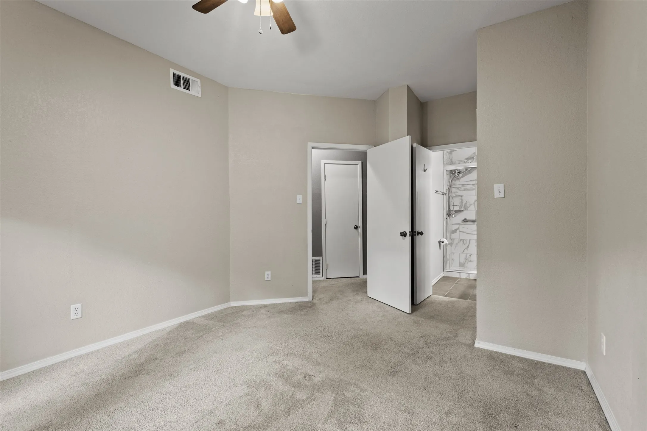 Spacious bedroom with neutral wall finishes, plush carpet flooring, ceiling fan with integrated lighting, and direct access to an ensuite bathroom featuring marble-look tile surround and glass-enclosed shower