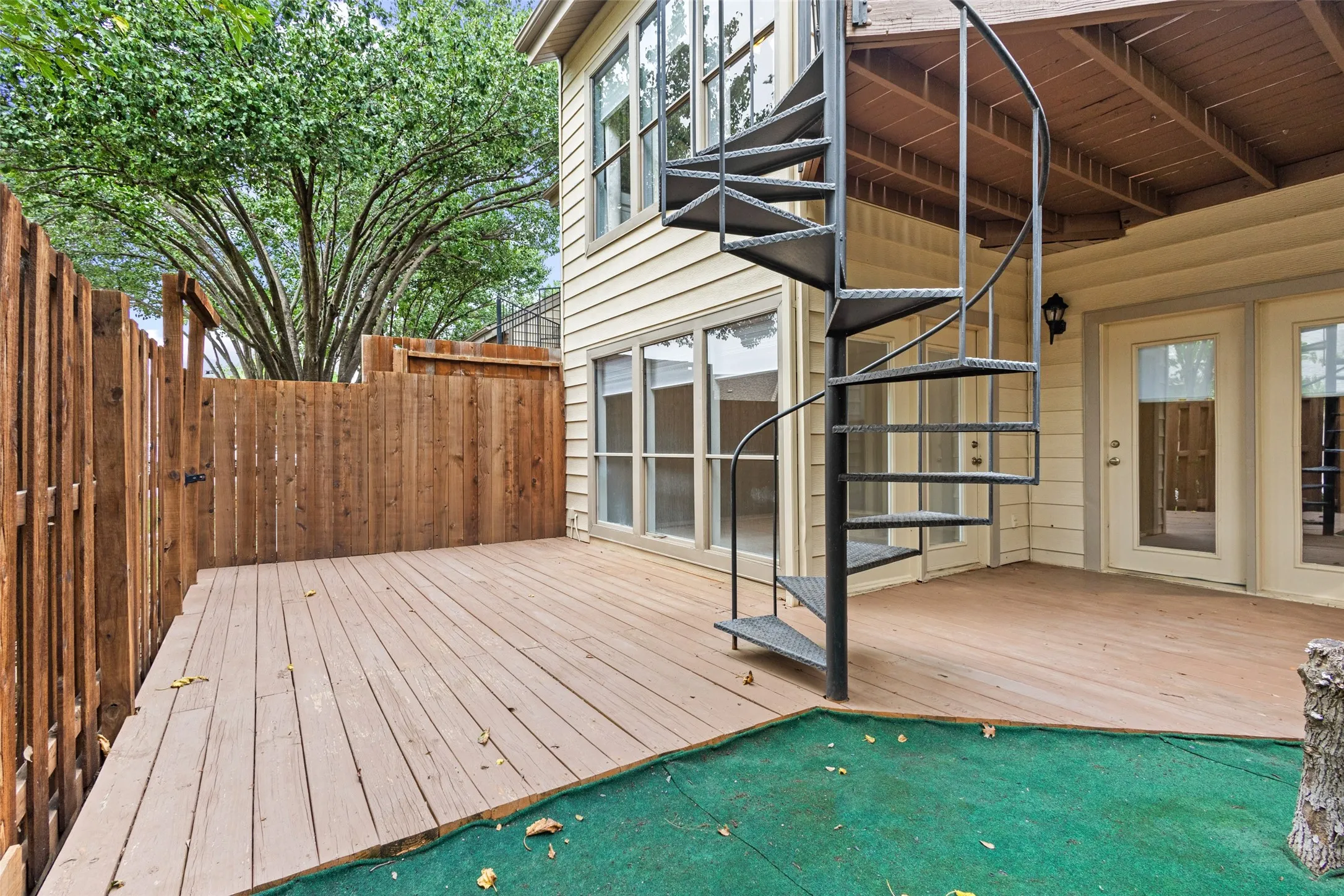 Expansive outdoor deck with a spiral staircase, wood fencing, and multiple exterior doors