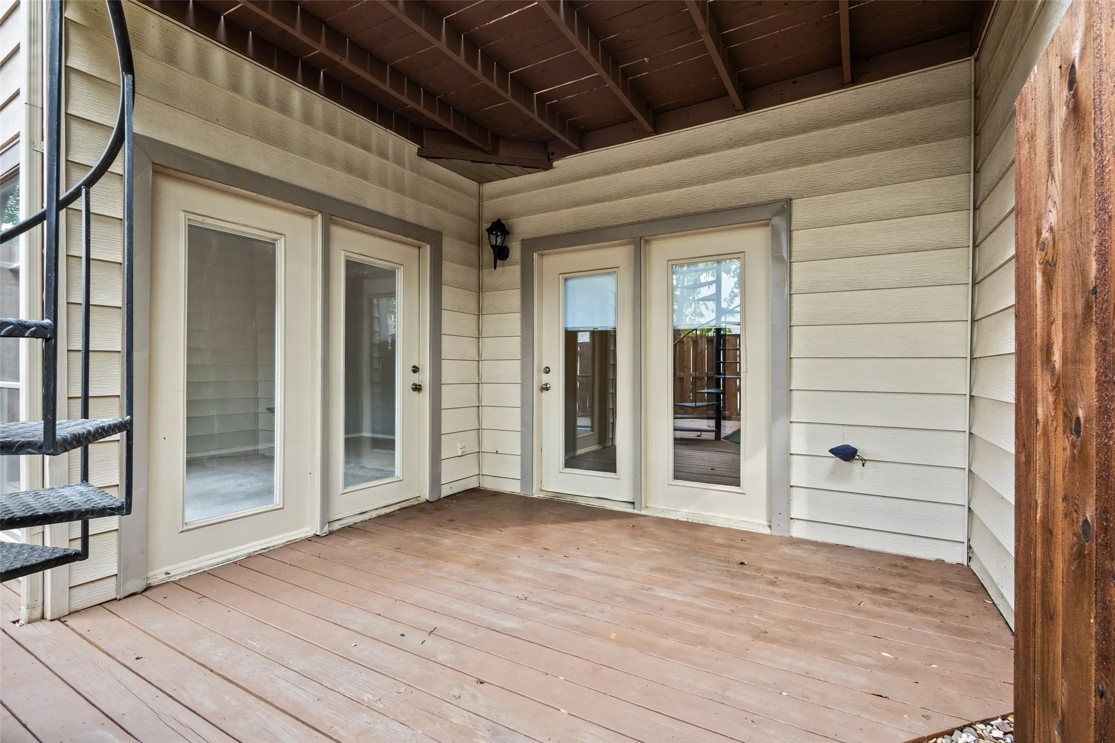 Expansive outdoor deck featuring wood-finish flooring, multiple glass-paneled doors, spiral staircase access, and siding exterior