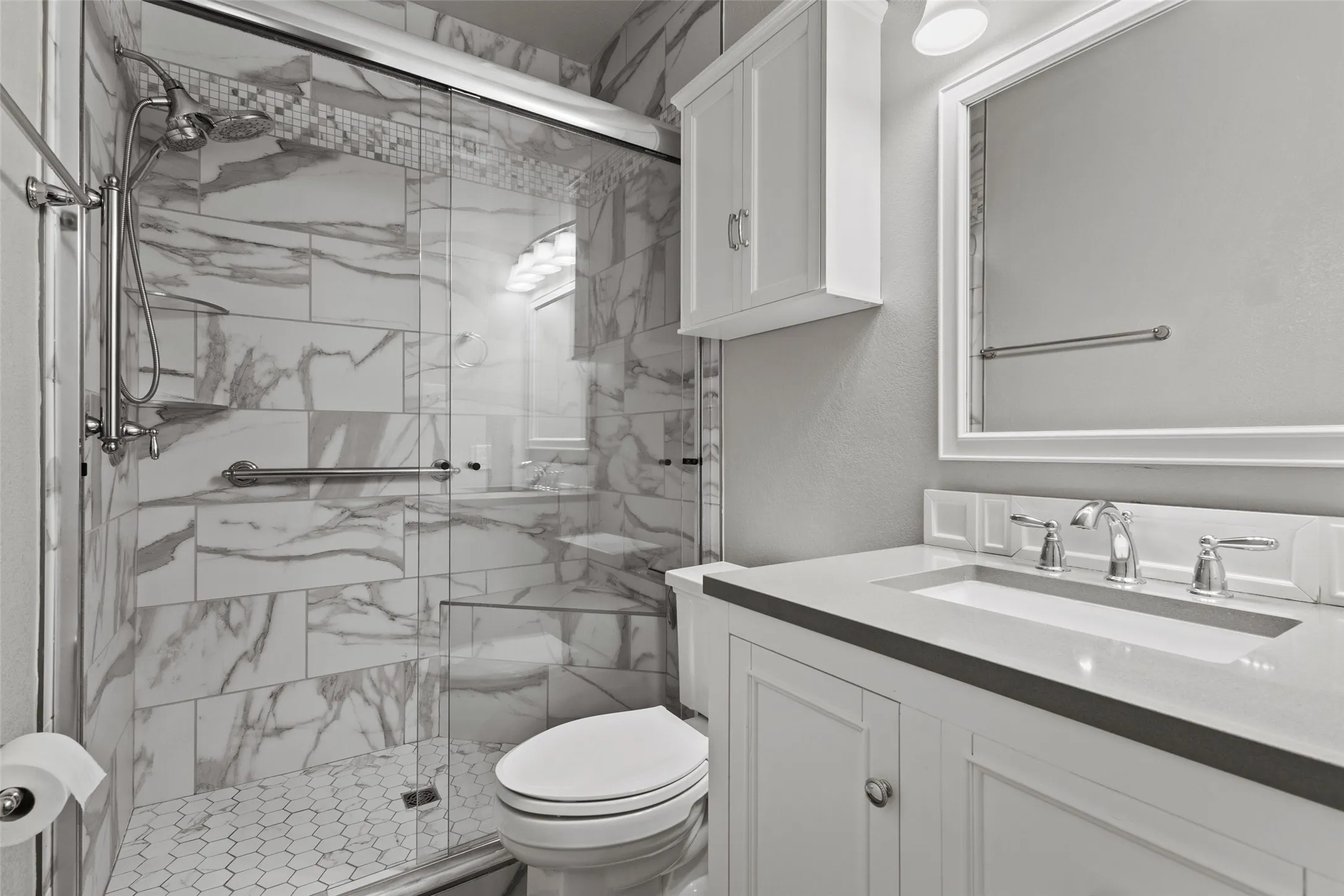 Walk-in shower with clear glass enclosure, marble-style tiled walls, and a hexagonal tiled floor
