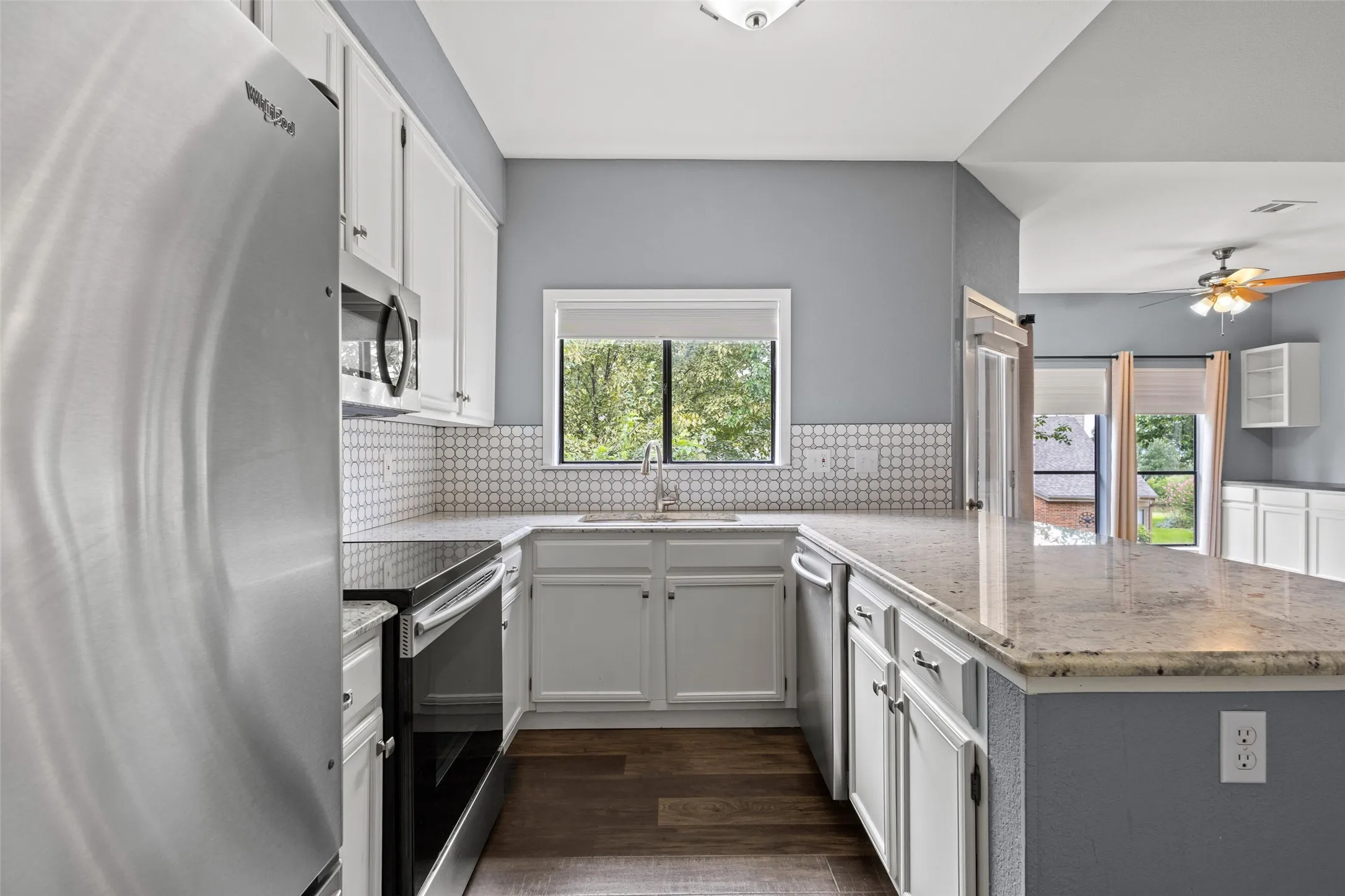 Stainless steel appliances, white cabinetry, a tile backsplash, wood-finish flooring, and light-toned countertops