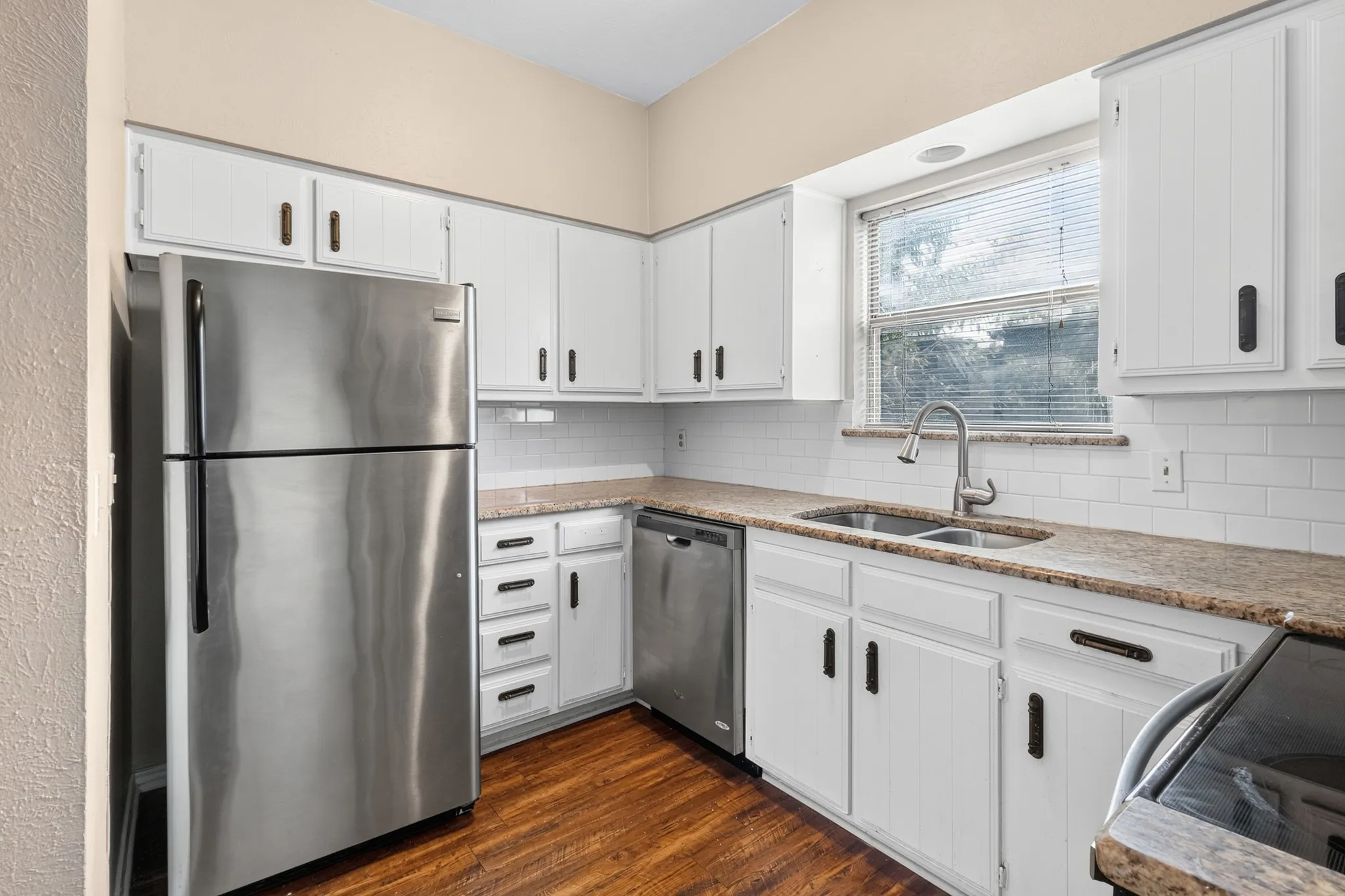 Kitchen featuring white cabinetry, stainless steel appliances, wood-finish flooring, subway tile backsplash, and a double basin sink with a gooseneck faucet