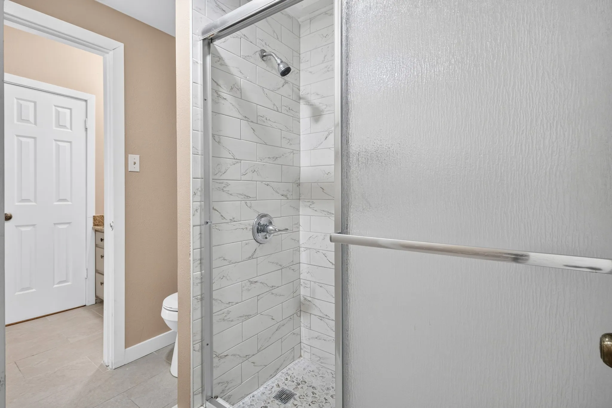 Shower enclosure with white subway tile surround, mosaic tile flooring, and polished chrome fixtures