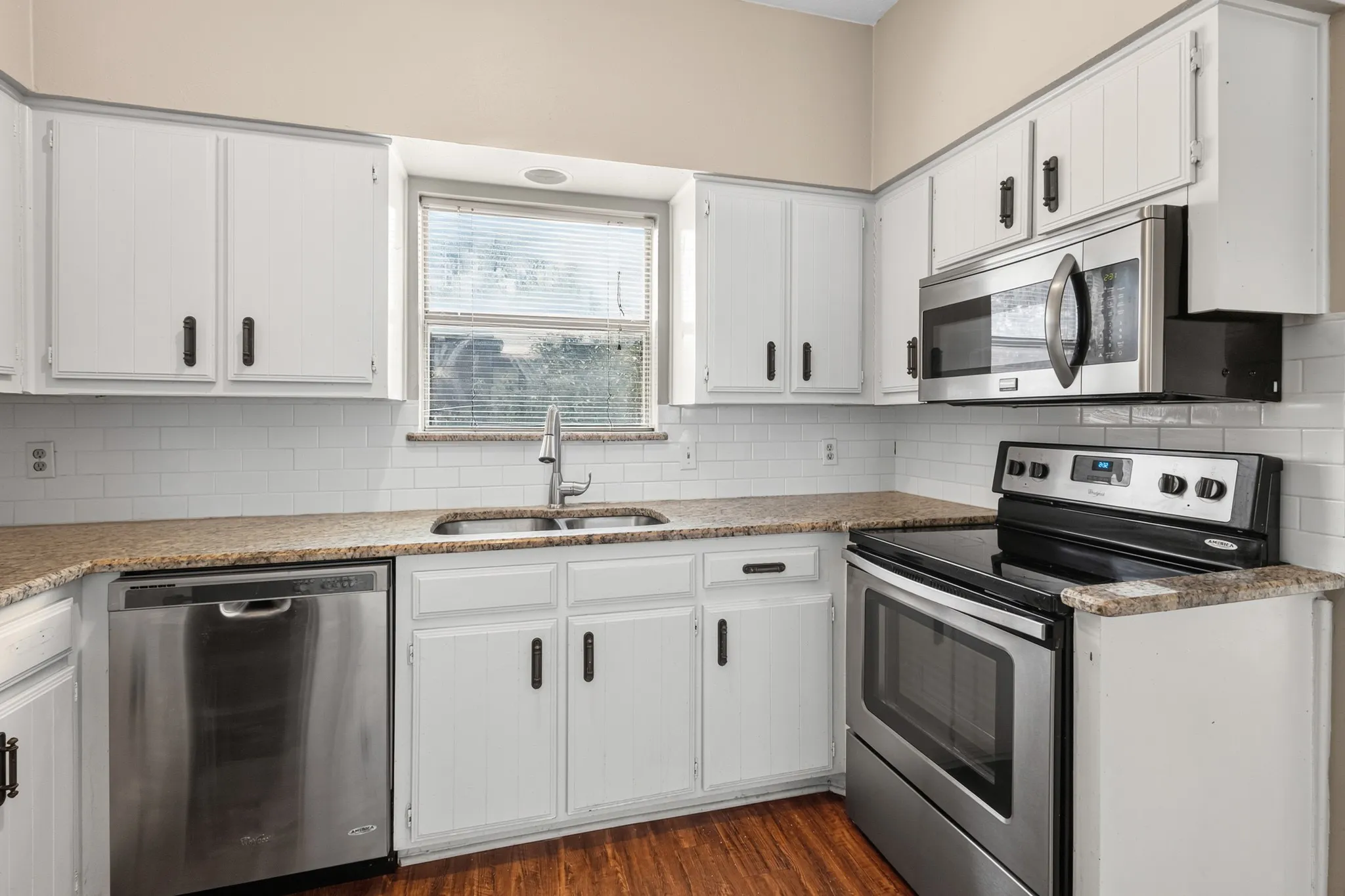 Kitchen featuring white cabinetry, stainless steel appliances, a subway tile backsplash, granite-finish countertops, and wood-finish flooring