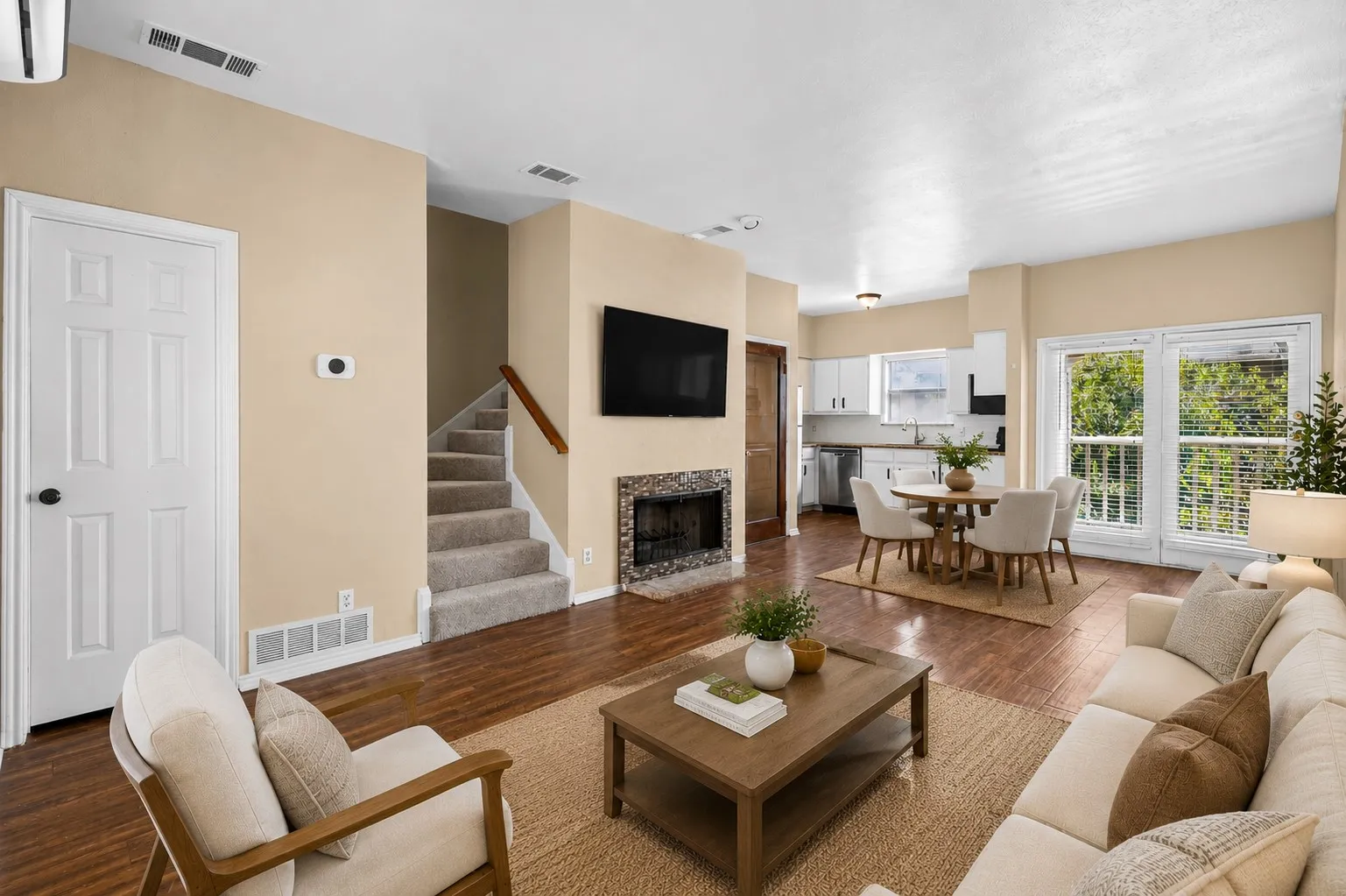 Wood-finish flooring, a tiled fireplace, and a kitchen with white cabinetry