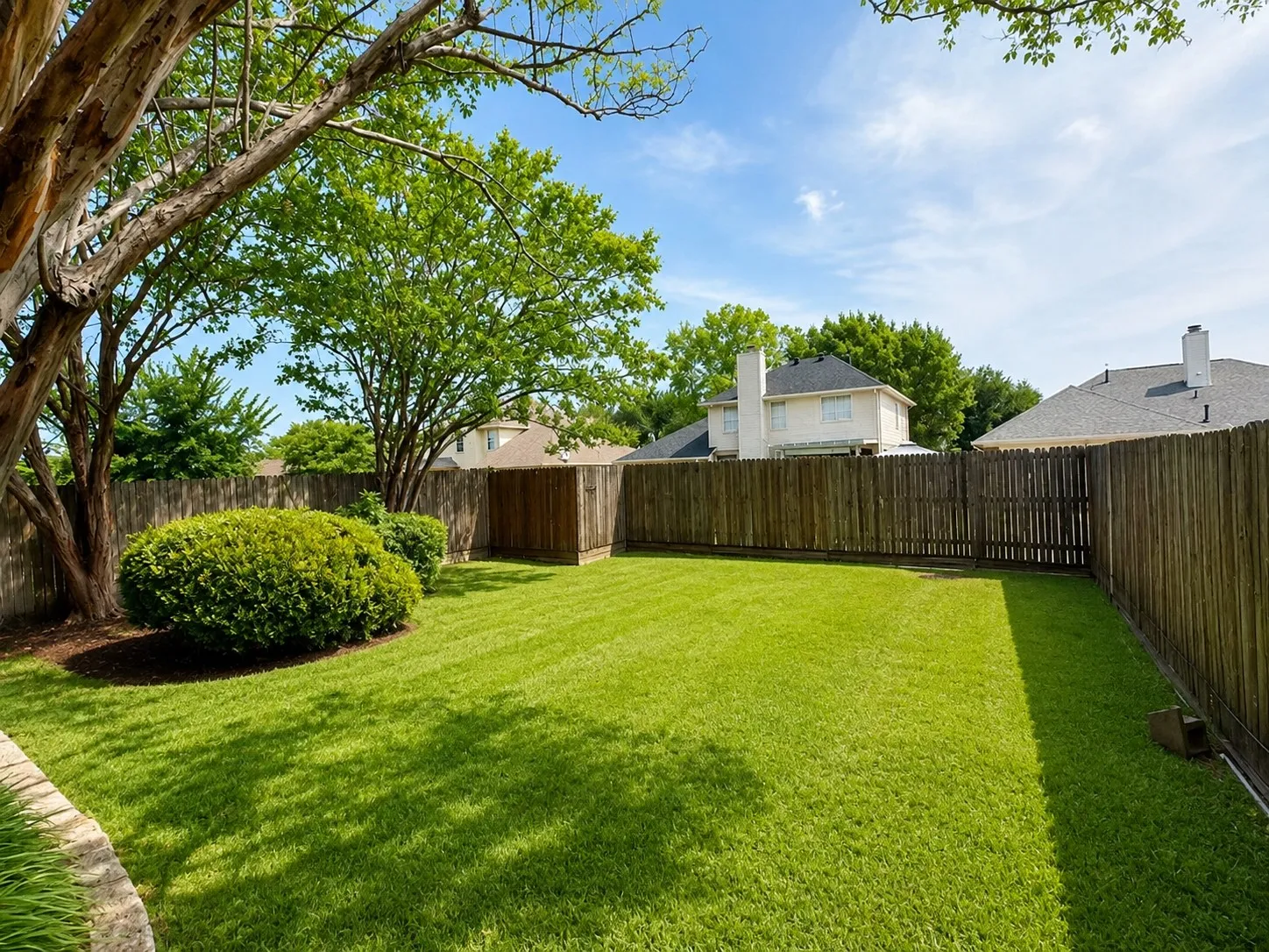 Expansive backyard featuring a lush lawn, mature trees, manicured shrubs, and a wood privacy fence