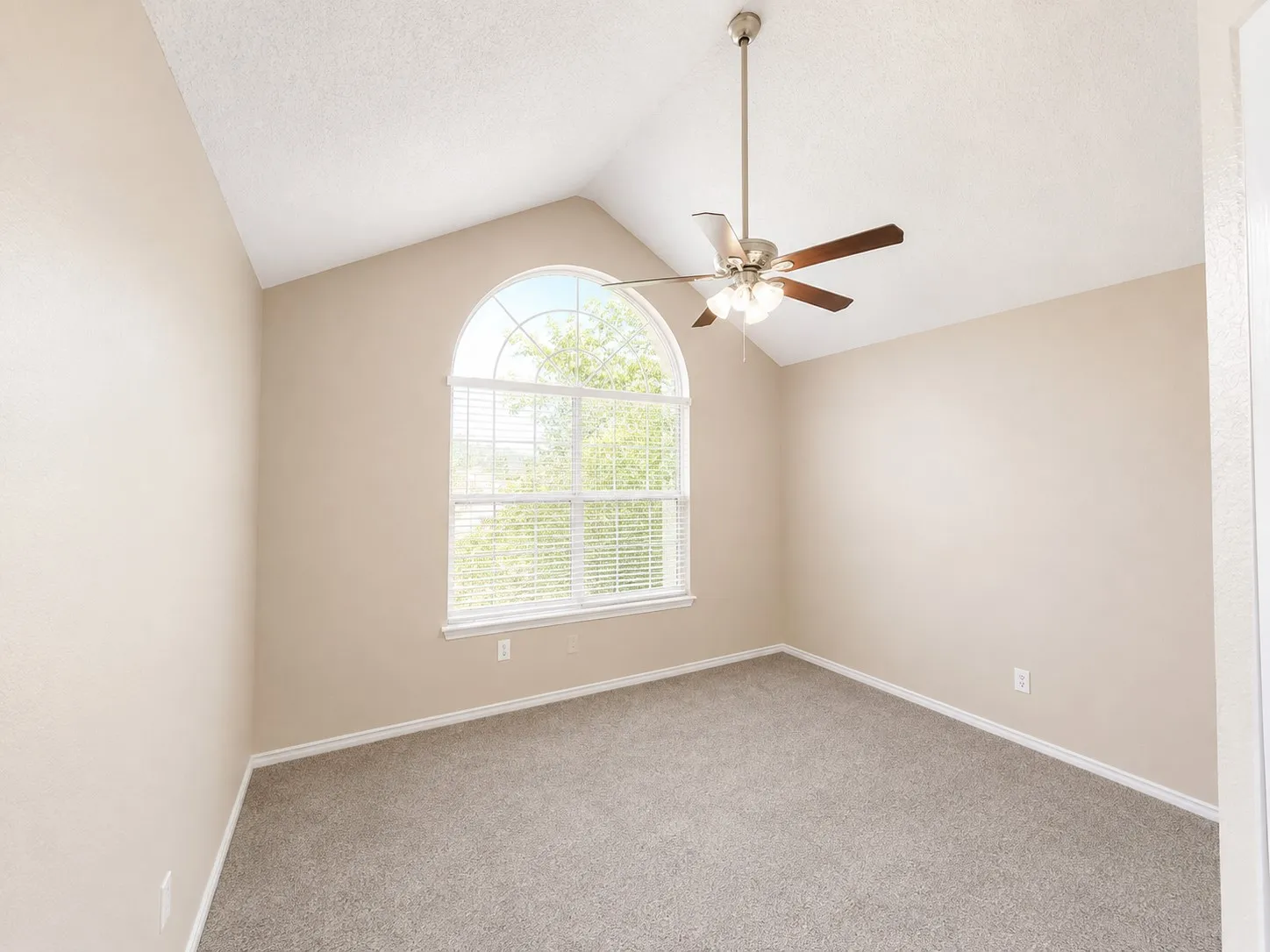 Arched window with blinds, vaulted ceiling, ceiling fan with light fixture, neutral wall paint, and gray carpet flooring