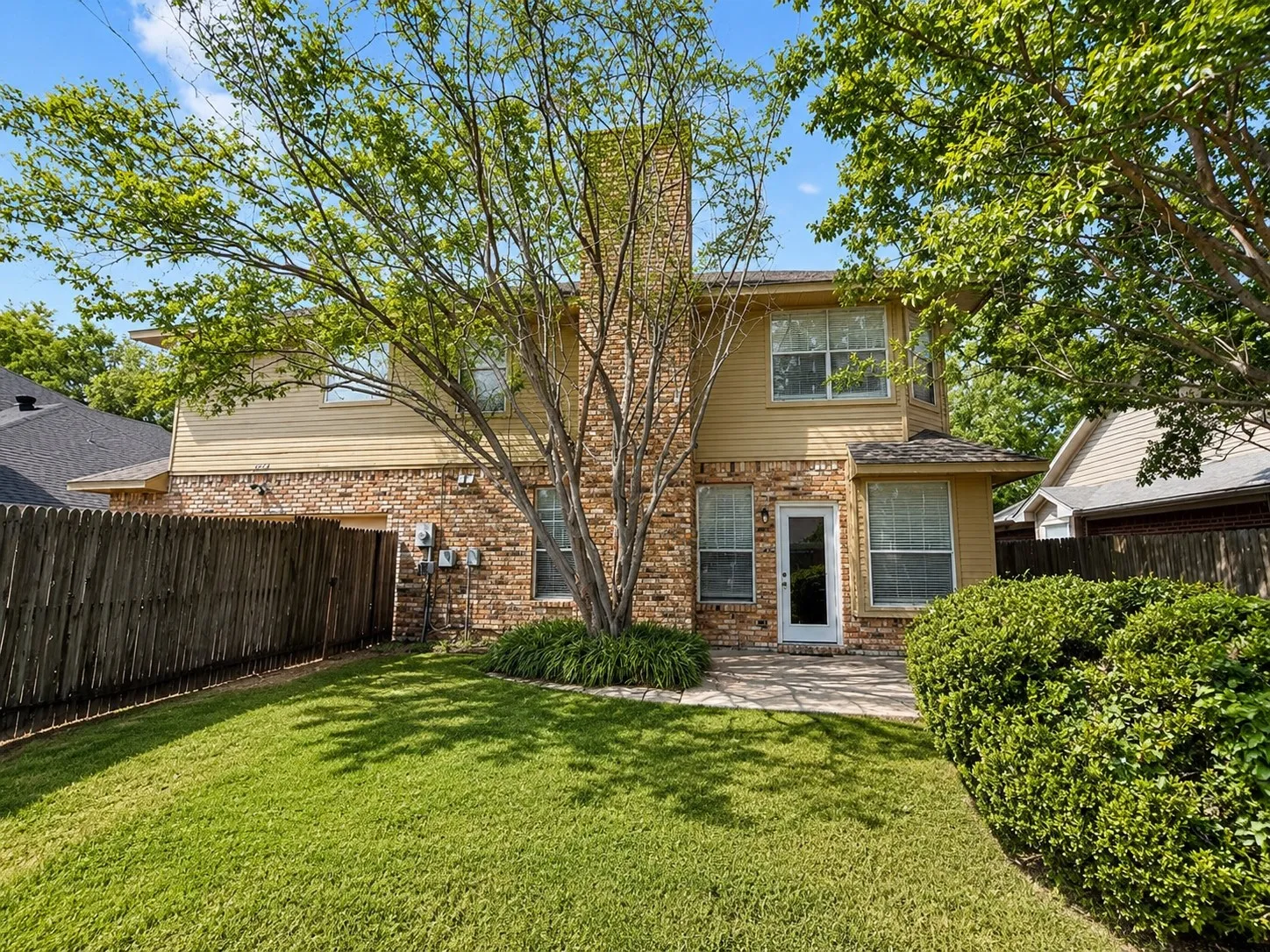 Expansive backyard featuring a manicured lawn, brick and siding exterior, brick chimney, and a paved patio area