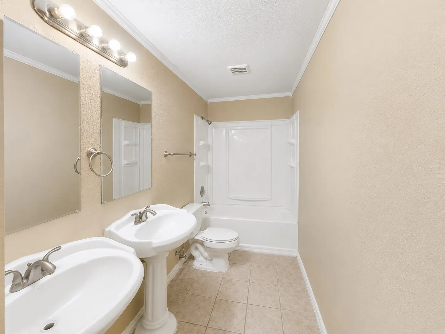 Bathroom featuring dual pedestal sinks, a combination tub and shower, brushed nickel fixtures, and tiled flooring
