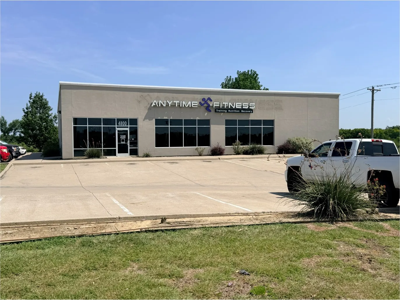 Single-story commercial building with a stucco exterior, large storefront windows, and a paved parking area